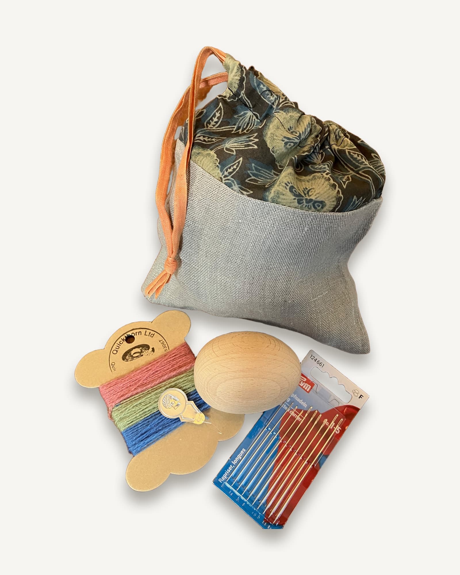 Light grey linen drawstring bag with orange cord, containing wooden darning egg, coloured wool on wooden bobbins