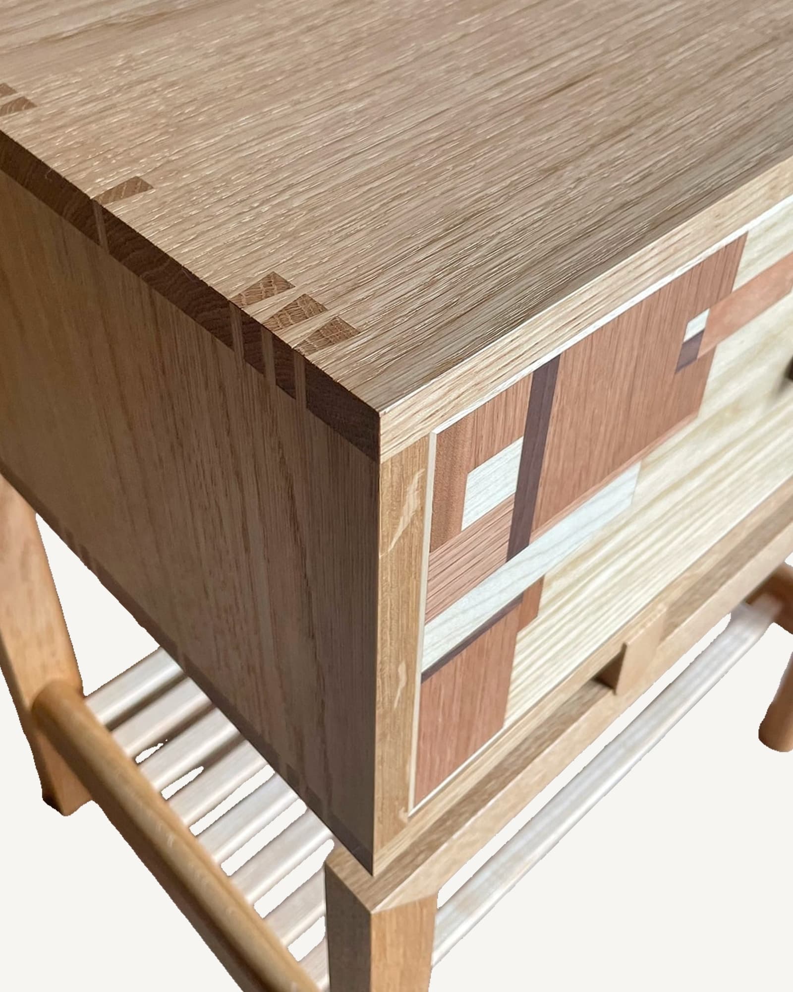 Oak and ash bedside table corner detail showing textured wood grain top, dark oak drawer with geometric marquetry inlay, and