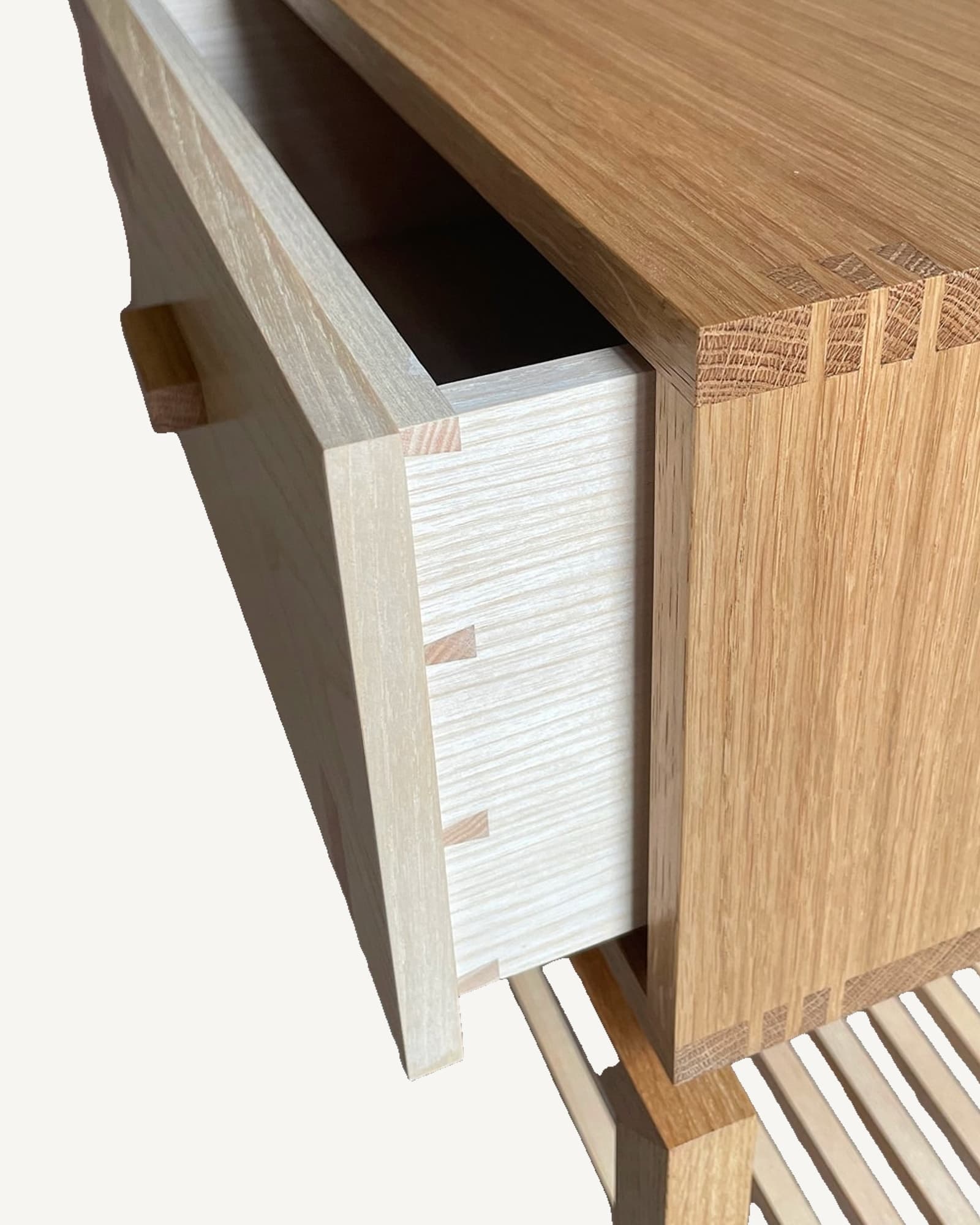 Partially open drawer of light oak bedside table with hand-cut ash marquetry front and wooden pull handle, revealing