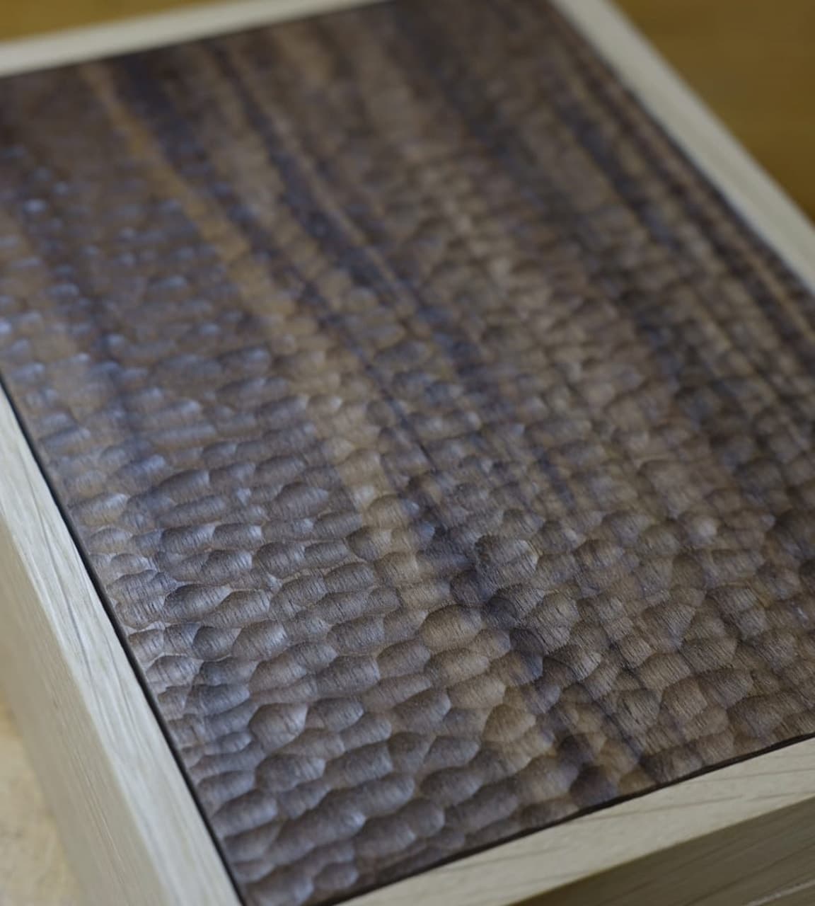 Close-up of a walnut panel hand-cut into rows of shallow scallops, framed by pale oak.