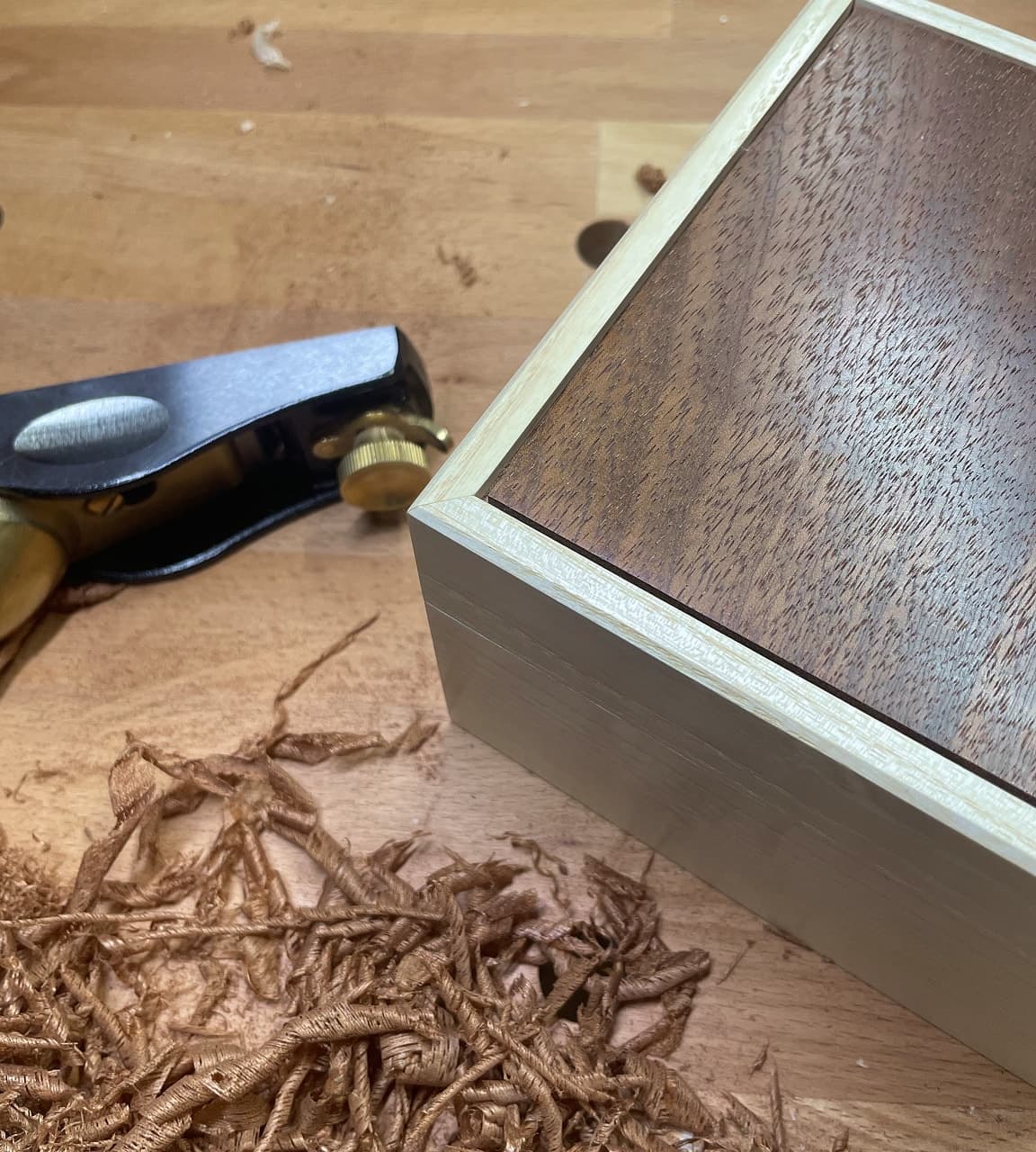 Angled view of rectangular box with pale ash frame and dark sapele lid, showing grain texture and silver-edged detail, with