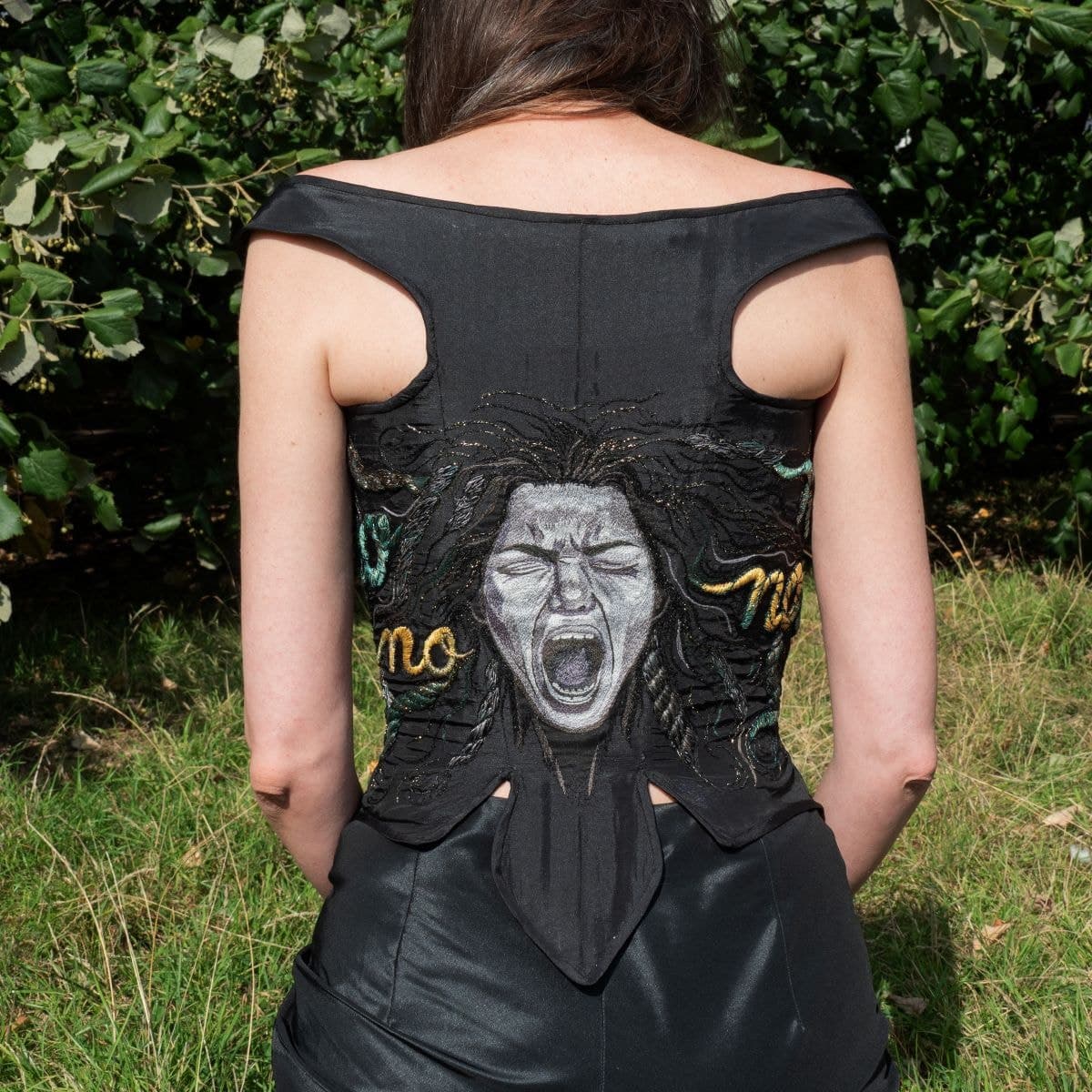 The corset worn, seen from behind, showing the embroidered Medusa face and hair in greyscale thread