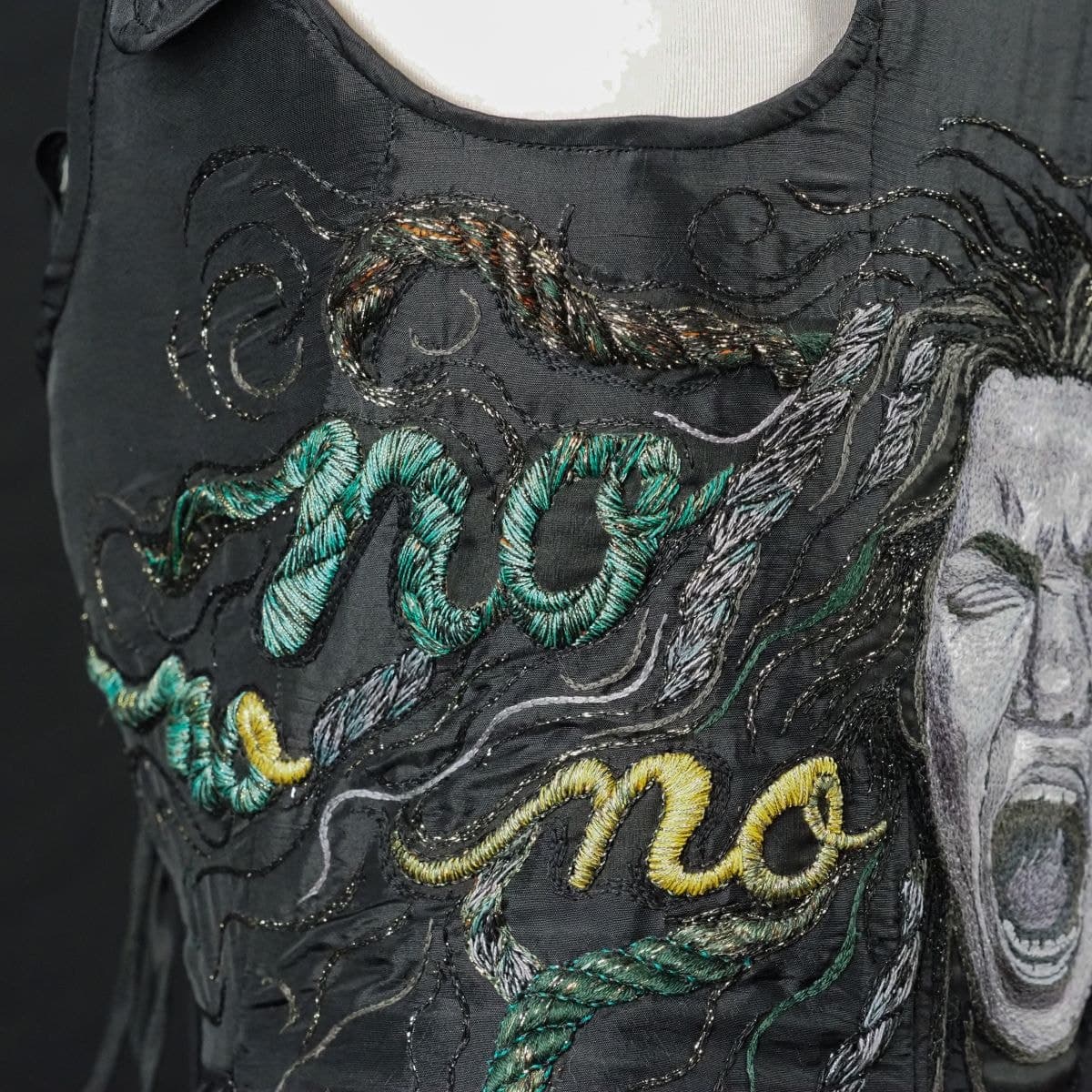 Detail of the word NO worked in green and gold cord within Medusa's embroidered hair
