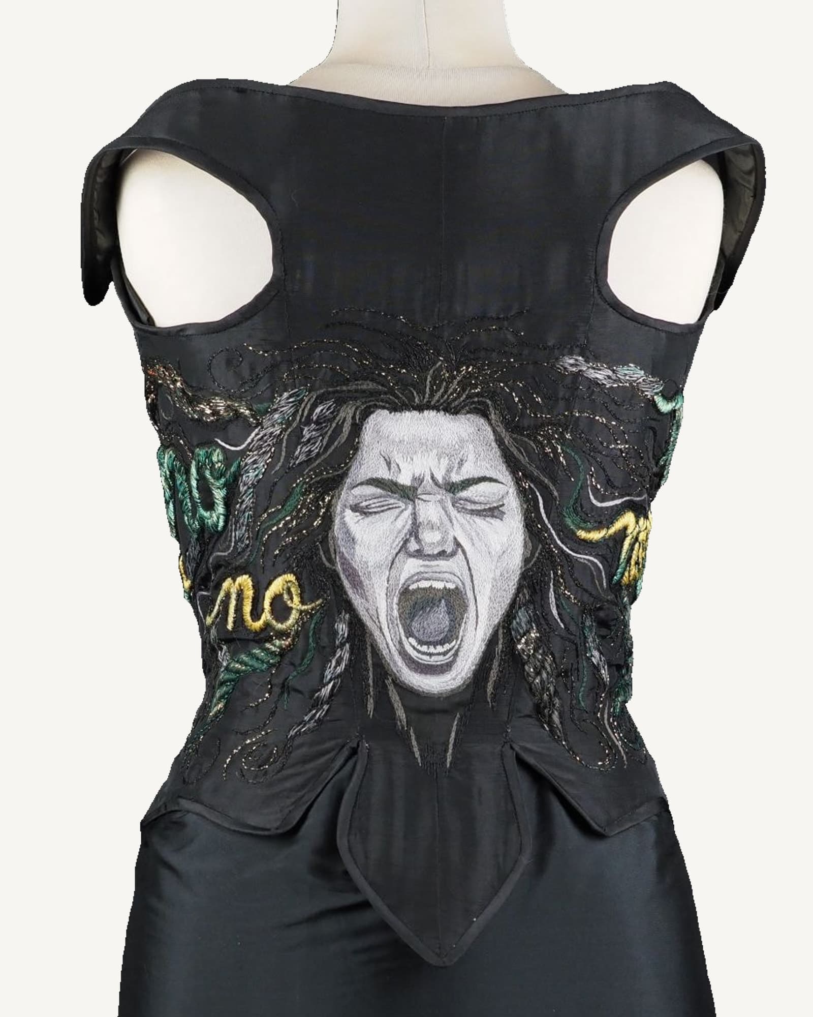 Black taffeta corset on a mannequin against black, its back embroidered with the face of Medusa