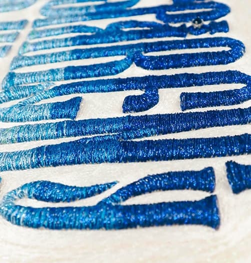 Detail of blue sequinned lettering raised above a pale stitched ground