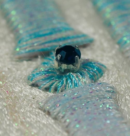 Close view of a blue stone set within turquoise sequin embroidery