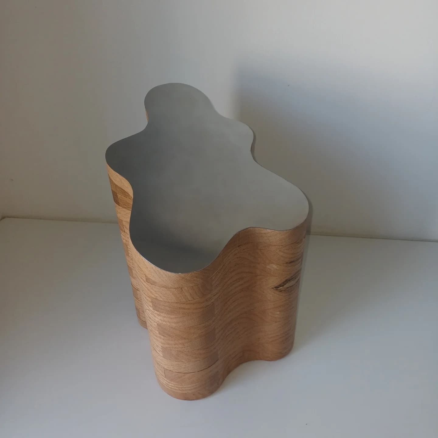 The urn from above, the shaped steel lid following the wave of the oak beneath it.
