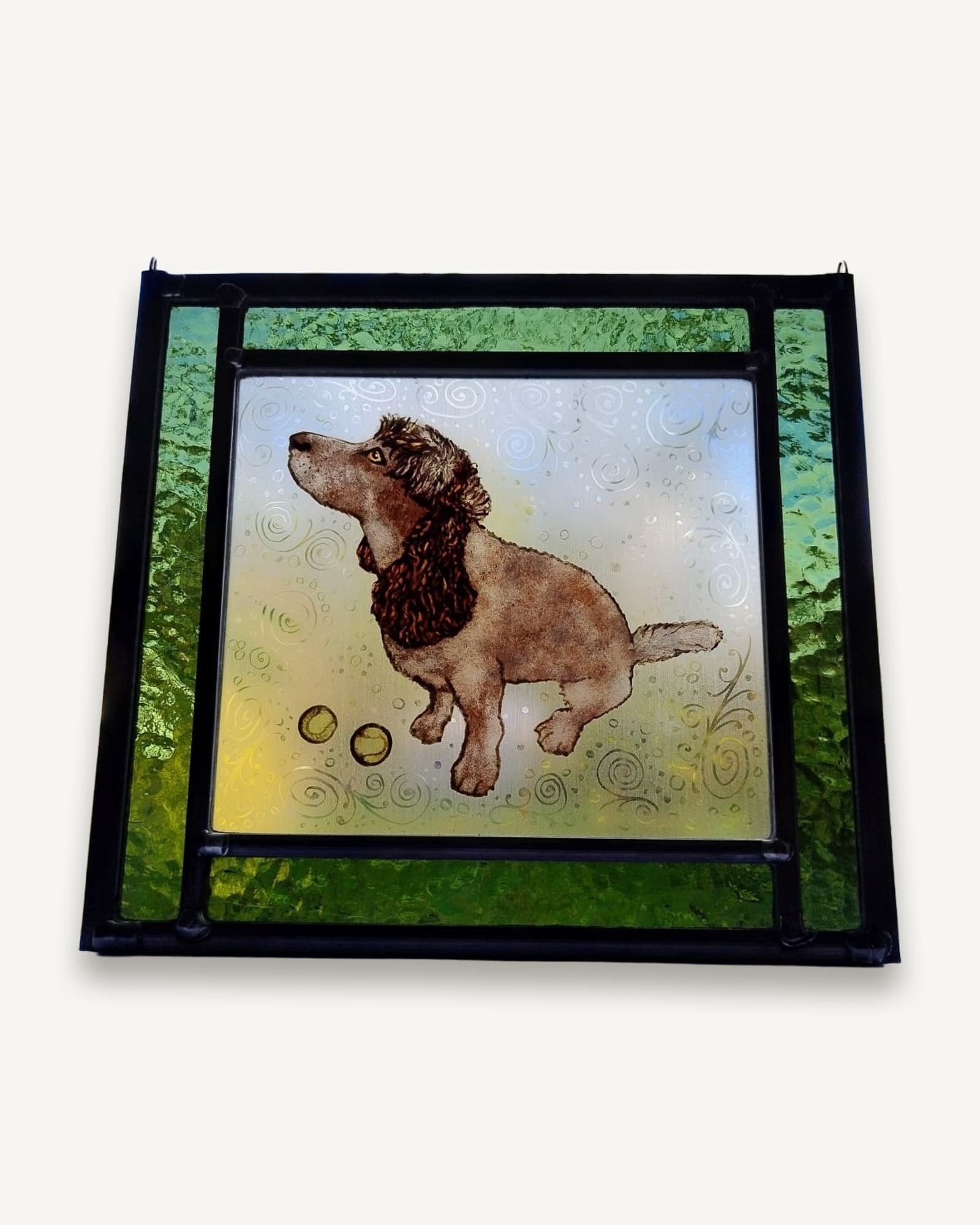 A spaniel painted onto textured glass and kiln-fired, framed in two tones of mottled green stained glass.