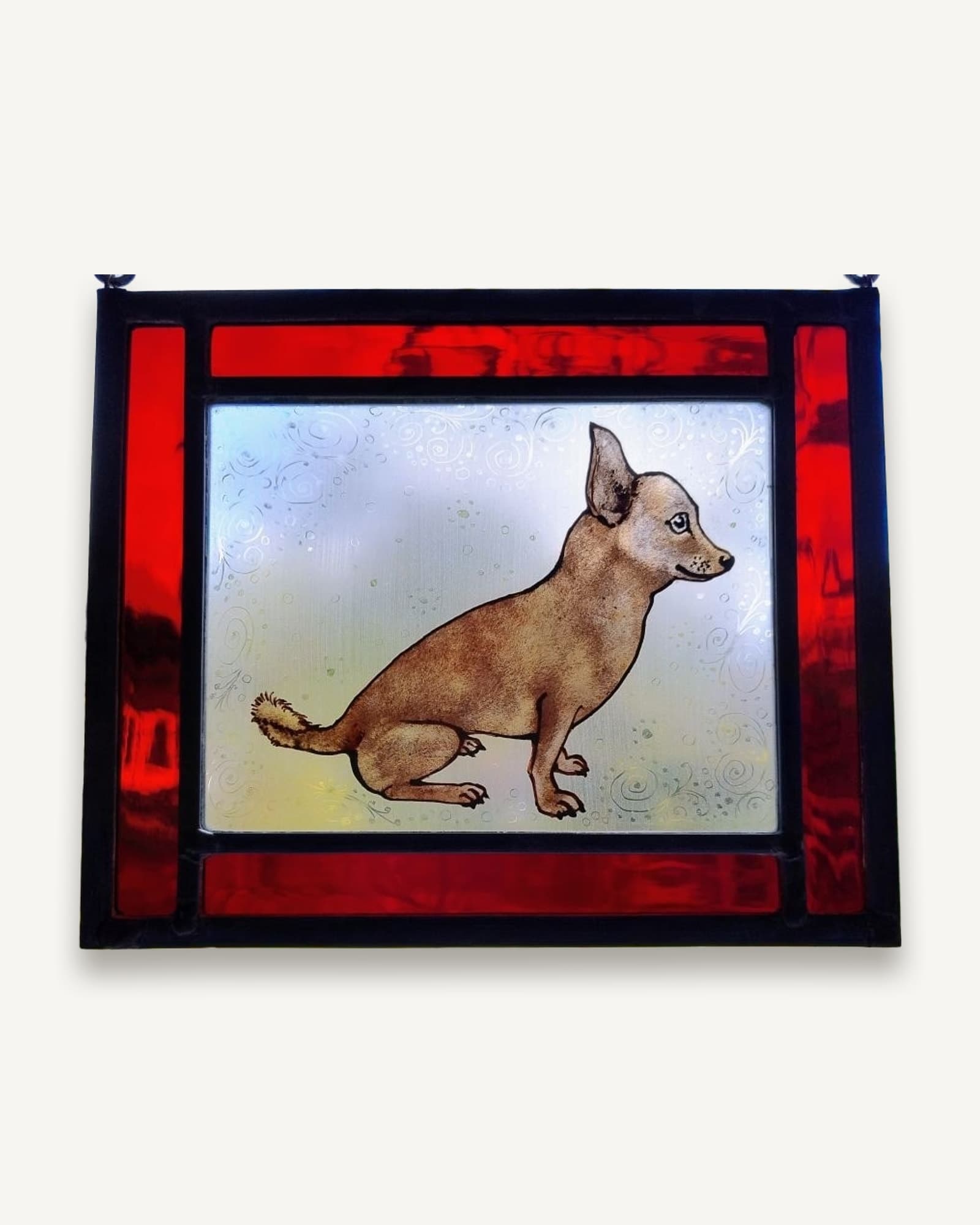 A chihuahua painted onto pale textured glass, framed on four sides in deep red stained glass.
