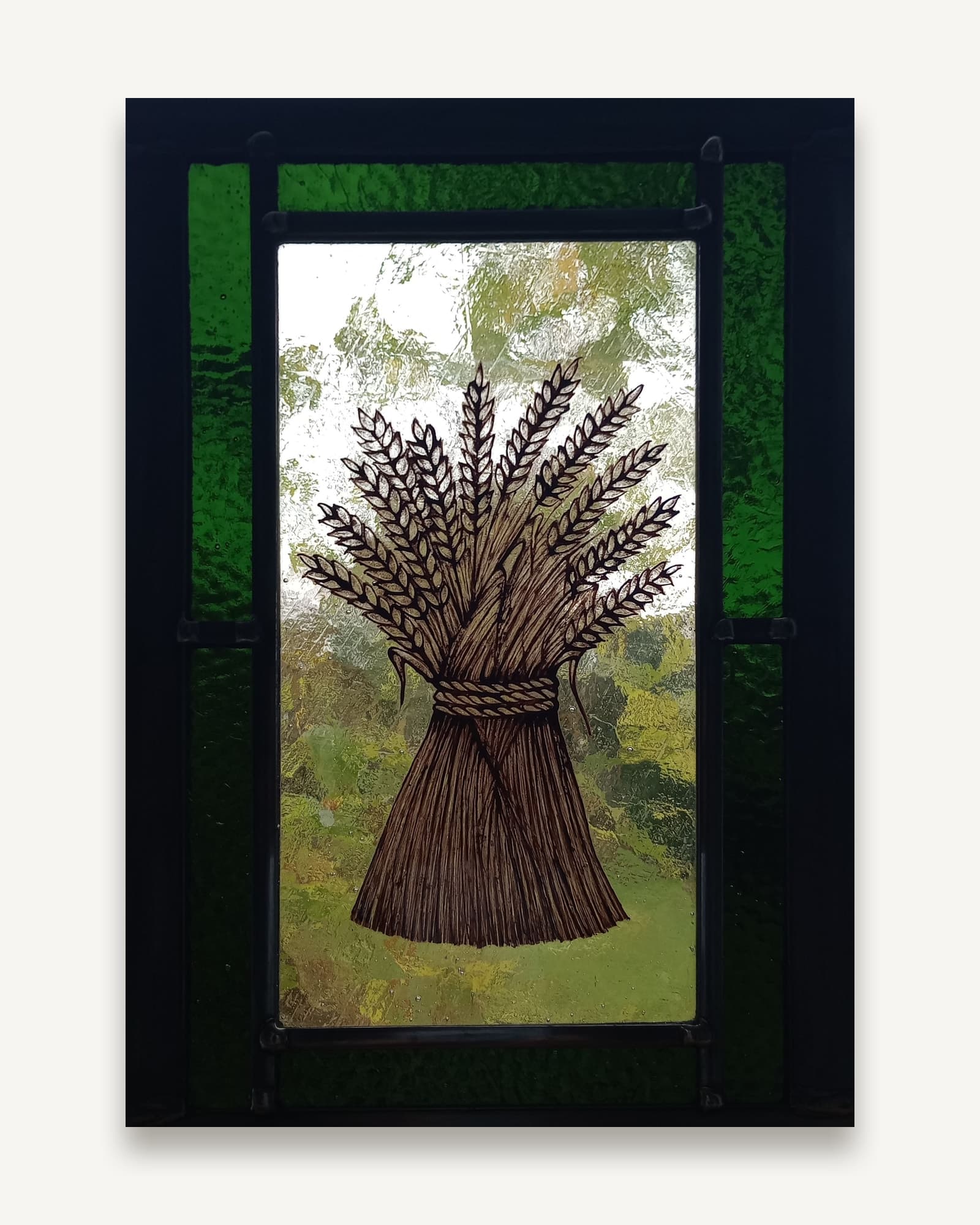 A bound sheaf of wheat painted in sepia onto pale glass, every ear drawn separately, set between green glass uprights.
