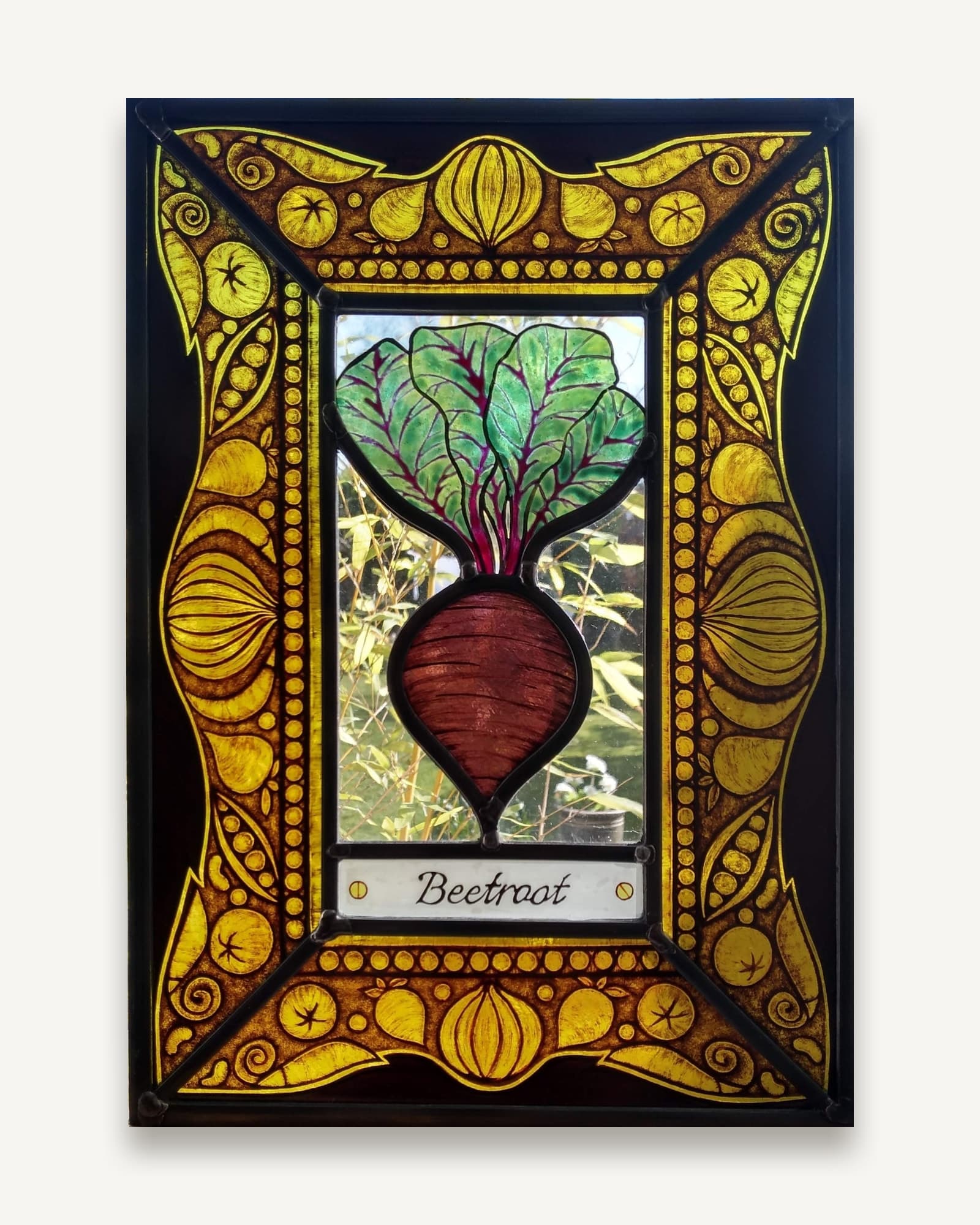 A stained glass kitchen garden panel: a painted beetroot over a nameplate, inside a deep amber border of stylised roots and seed heads.
