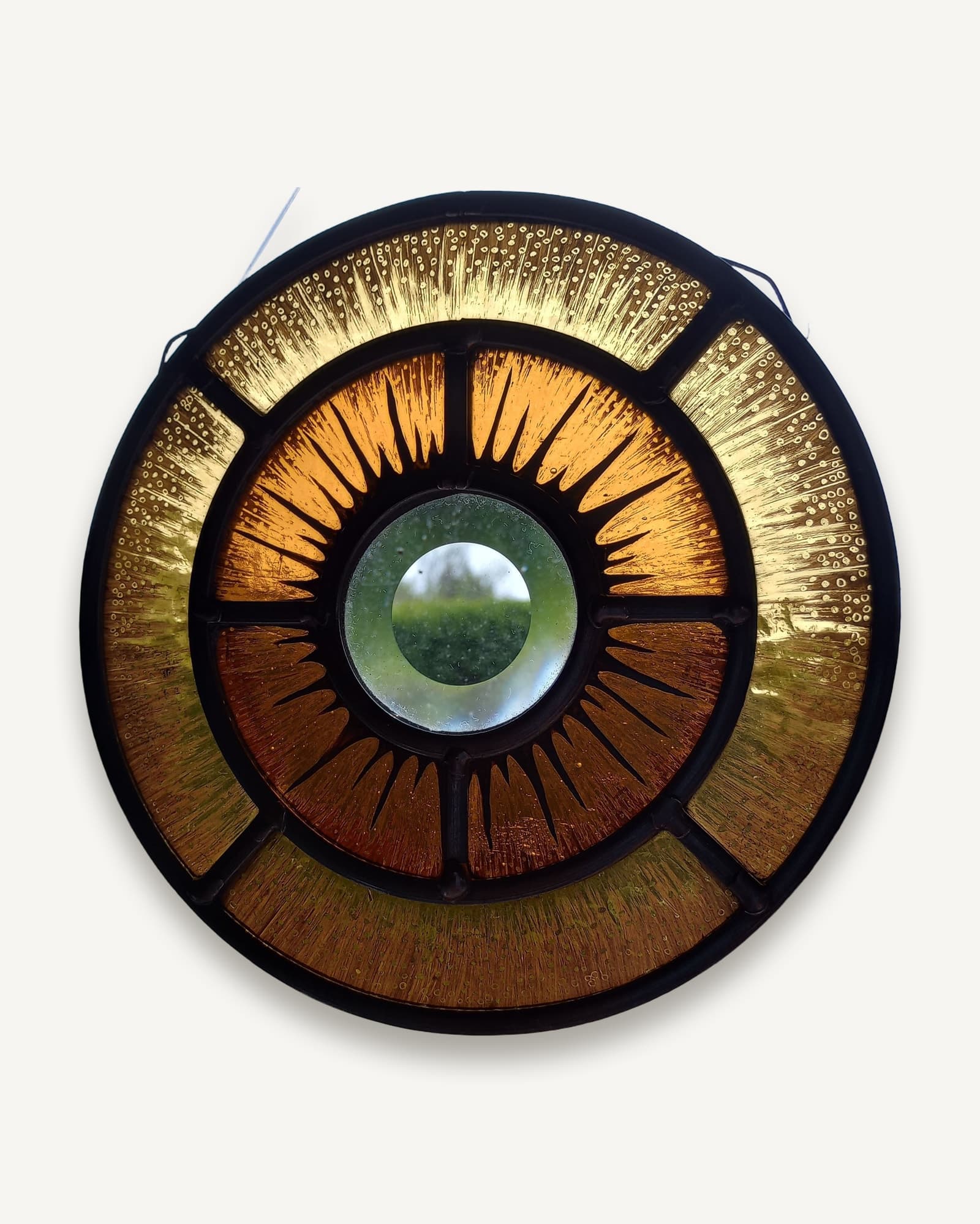 A circular leaded stained glass panel, amber and gold segments radiating from a clear bullseye rondel at the centre.