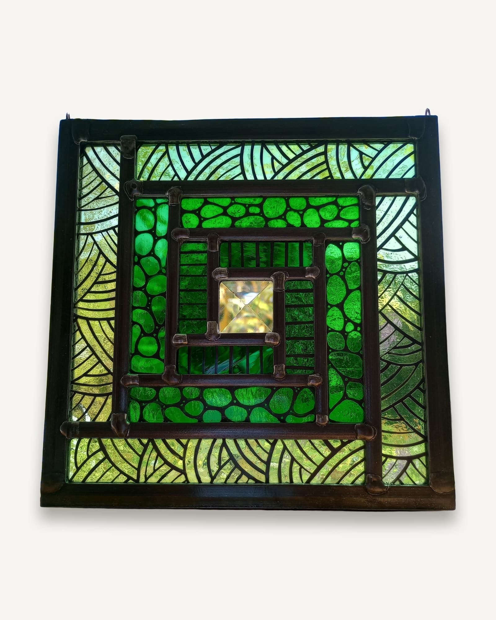 A square stained glass panel of concentric green bands painted with dots and leaf forms, turning on a clear bevel.