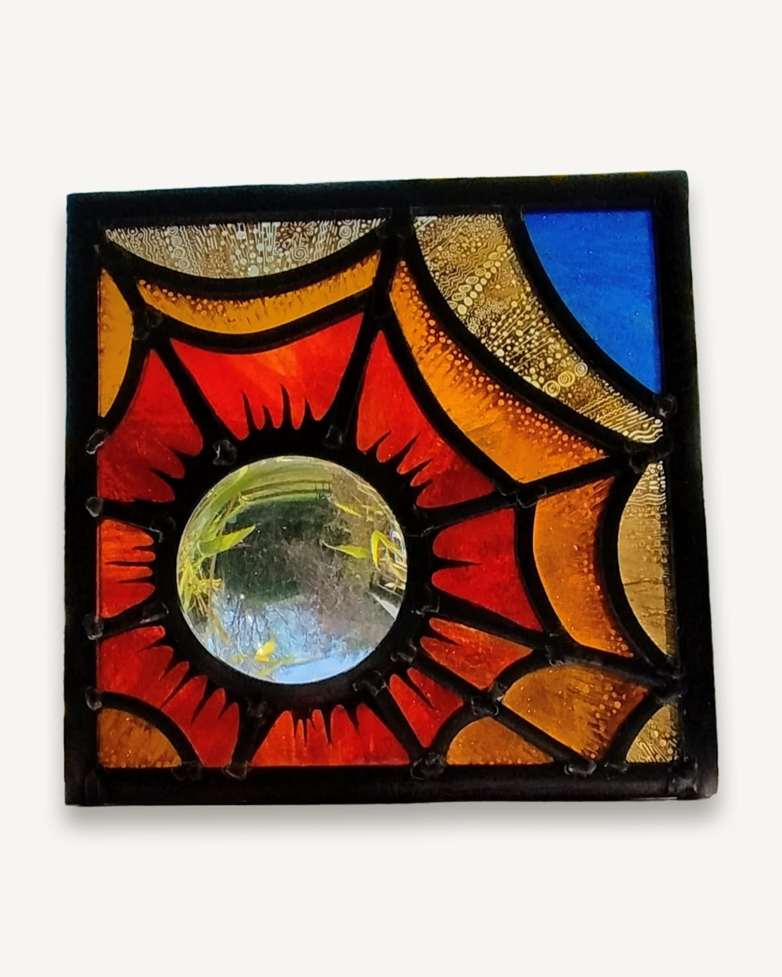 A square stained glass panel of reds, oranges and amber radiating from a clear central rondel like a struck flame.