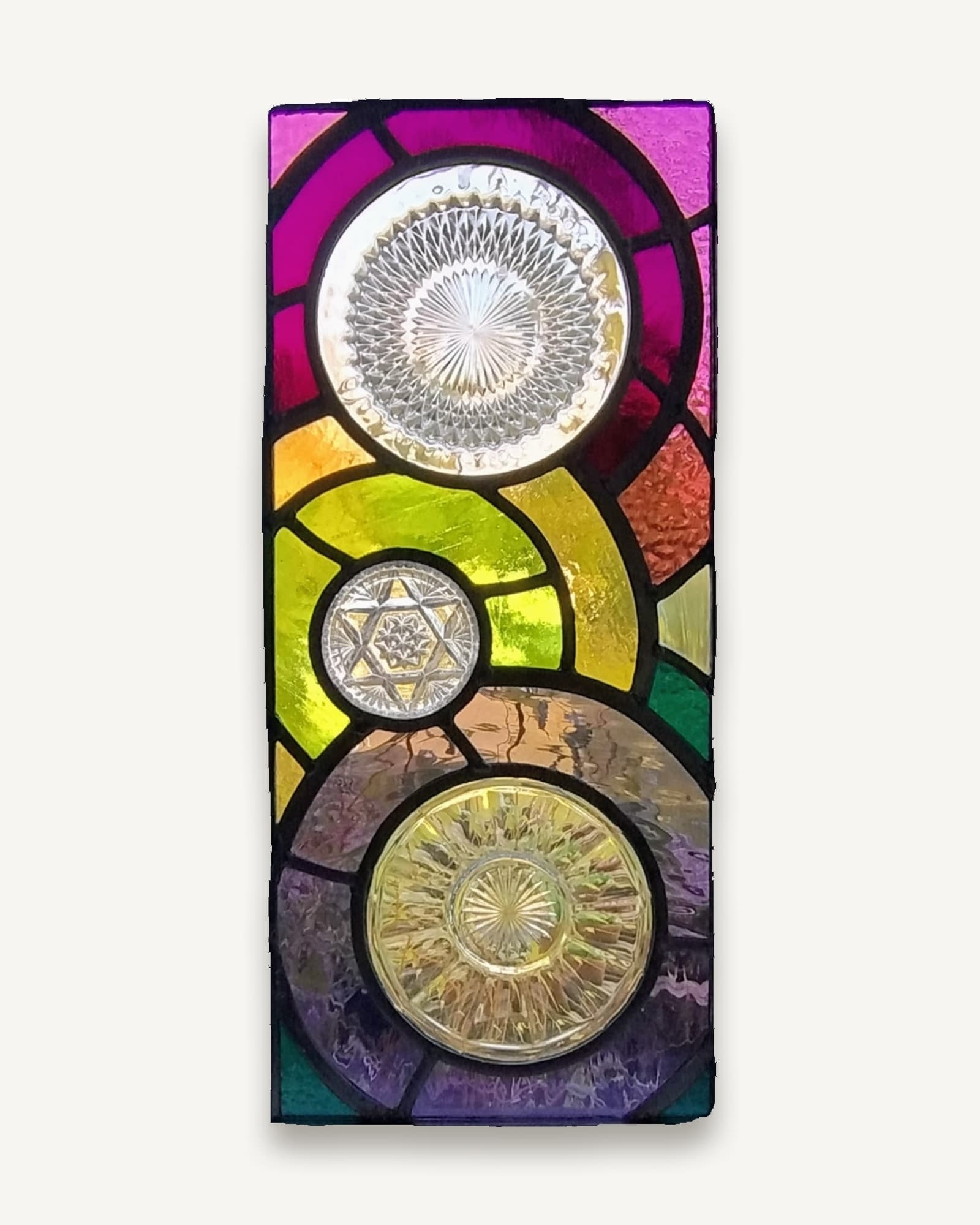 A tall narrow leaded panel with three vintage pressed-glass plates stacked vertically on magenta, purple and gold glass.