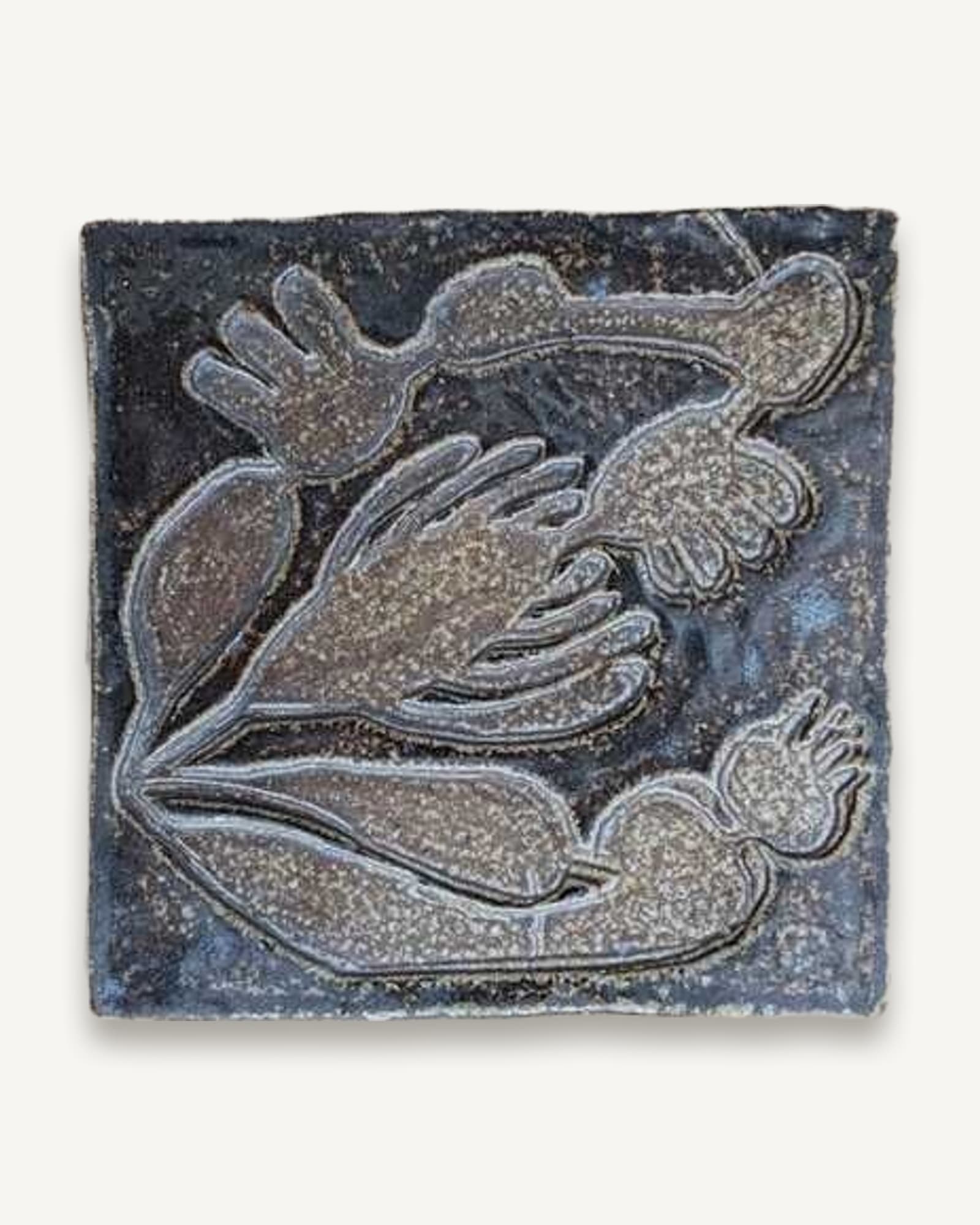 A salt-fired ceramic tile with an inlaid leaf and hand design, resting on wood