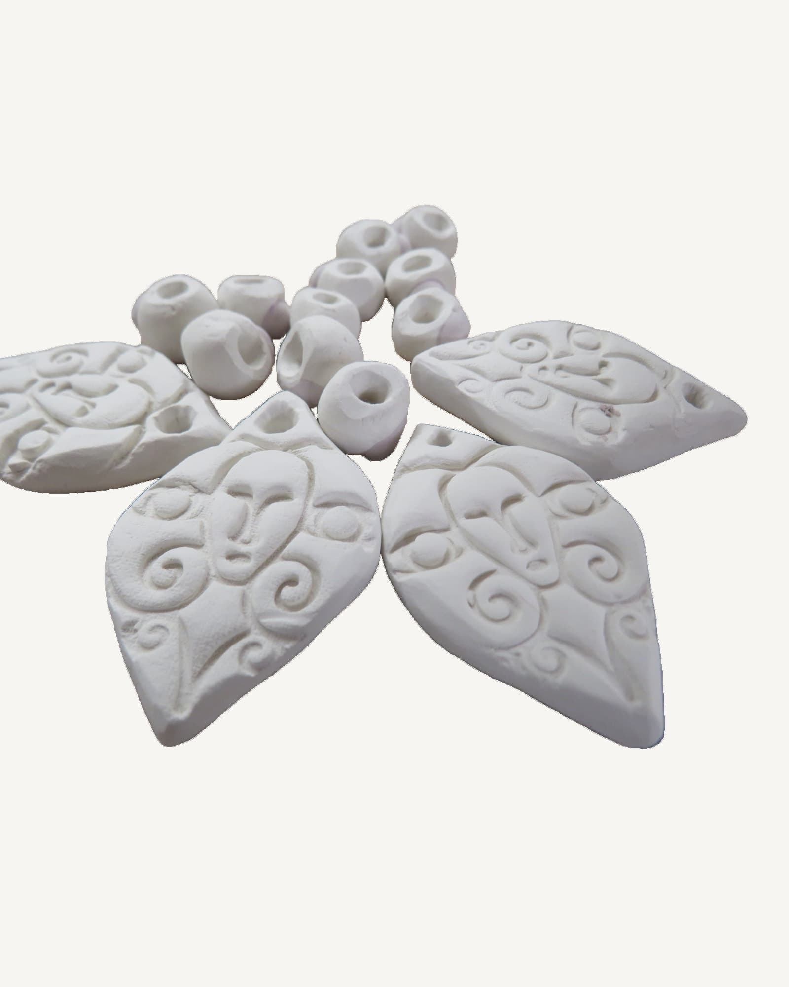 Unfired white porcelain charms stamped with faces and knotwork, laid on a board