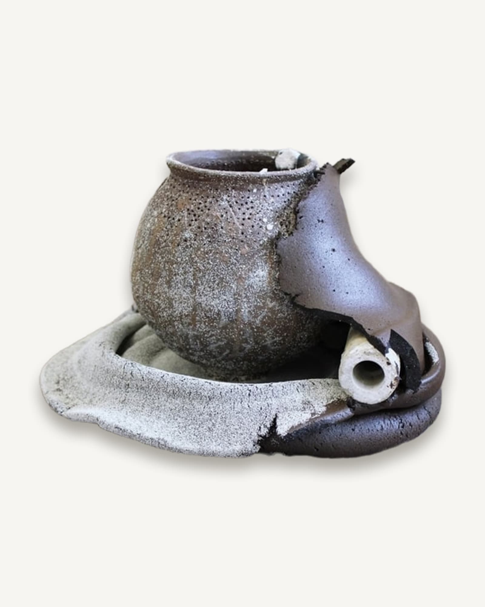 A dark wood-fired vessel resting in a pale ceramic cradle