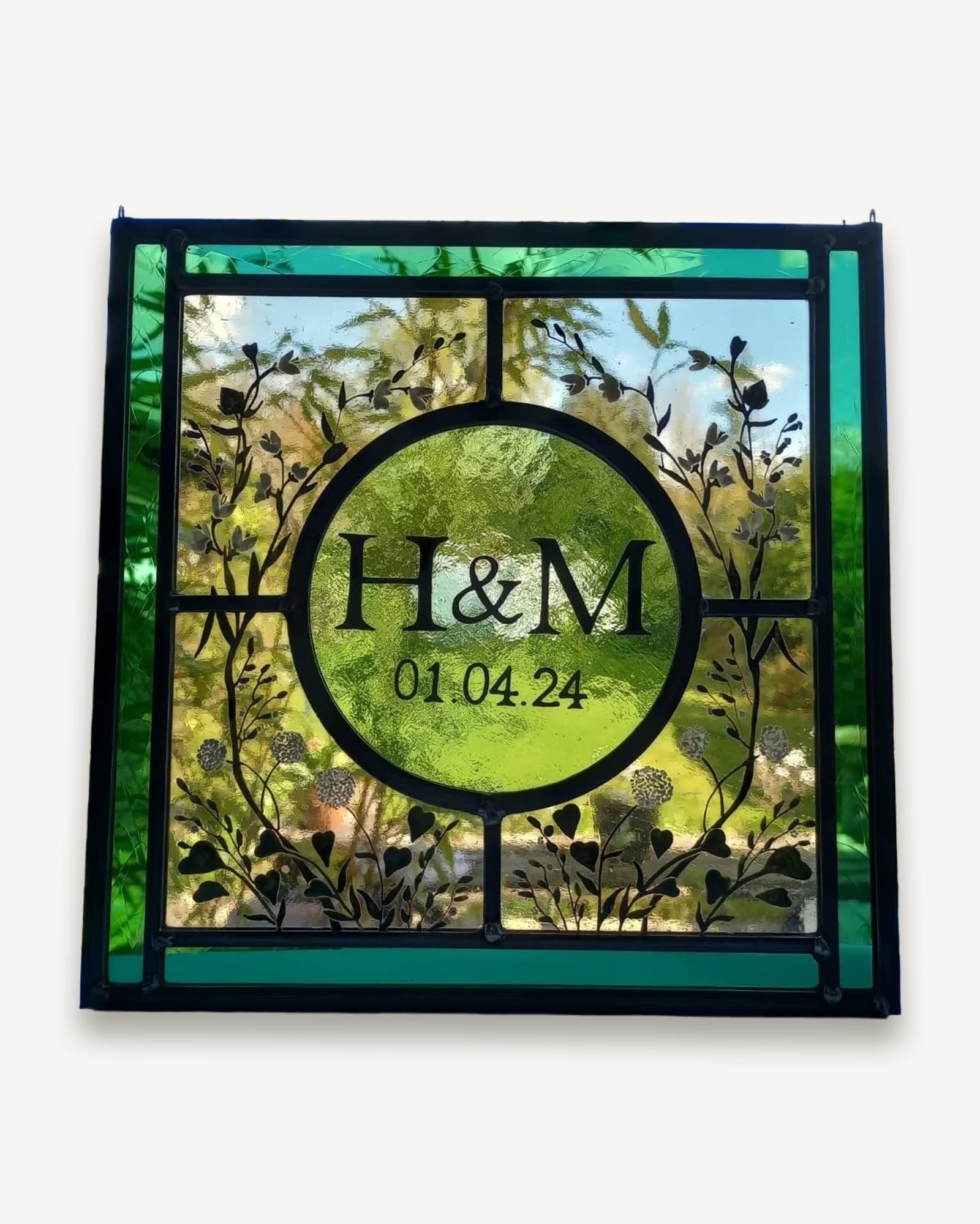 A stained glass wedding commission: initials and date in a painted circle wreathed in leaves, on green glass.