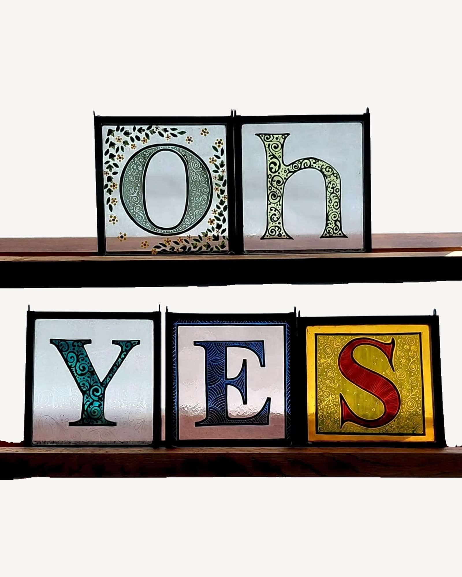 Individual letters painted in the manner of an illuminated manuscript, each leaded as its own small glass panel.