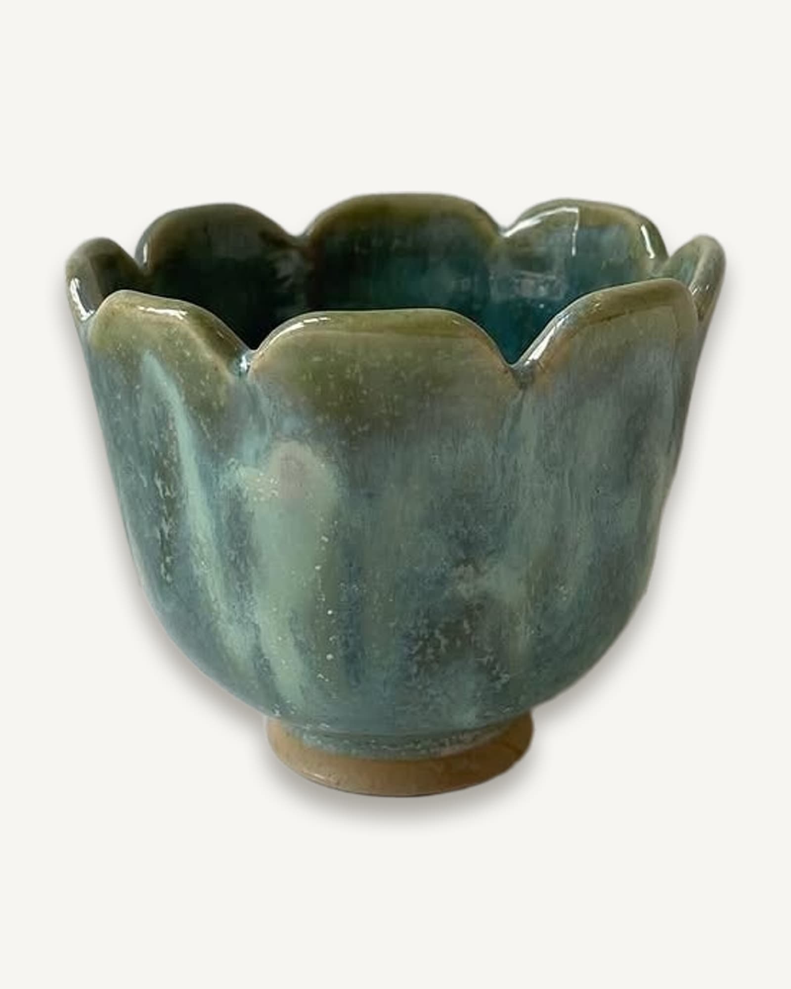 Small ceramic tulip cup with scalloped rim, turquoise-green glaze thinning to cream on petal edges, unglazed foot.