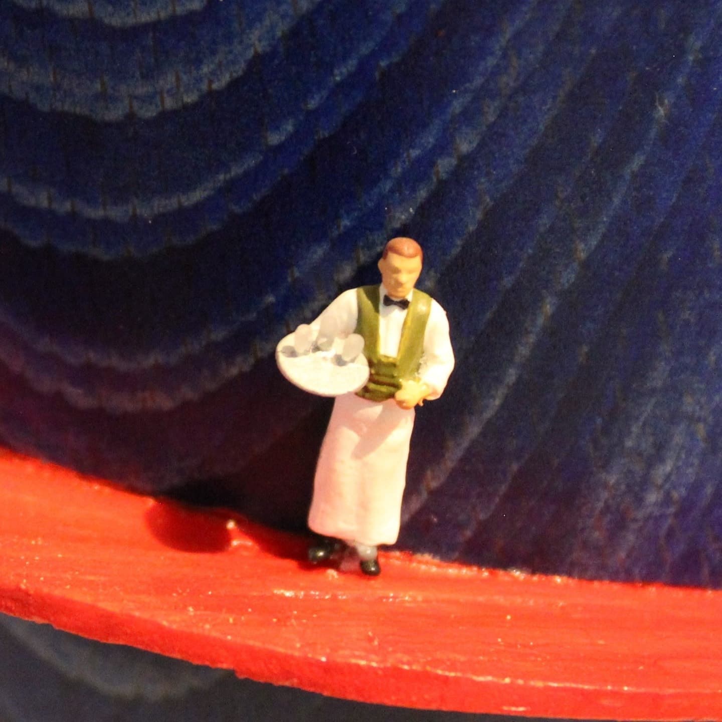 Small model figure of a man in an olive waistcoat holding a white plate