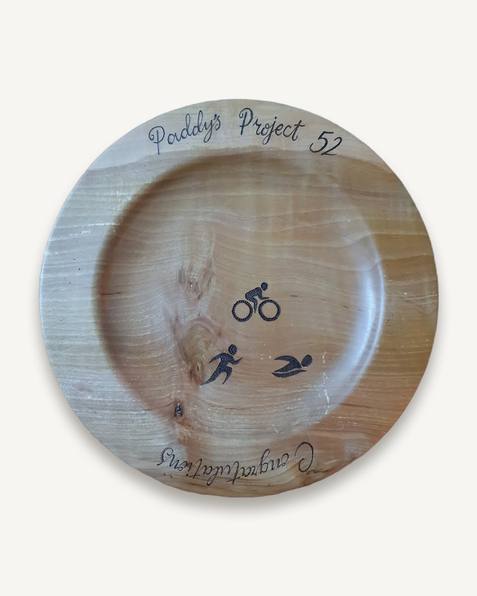 Turned pale wooden platter burned with cyclist, runner and swimmer figures and a handwritten congratulation