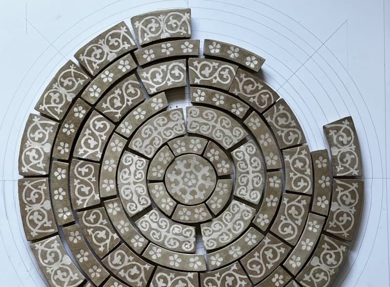 Unfired curved tiles laid out in rings on a paper template, inlaid with white scrolls and flowers before firing