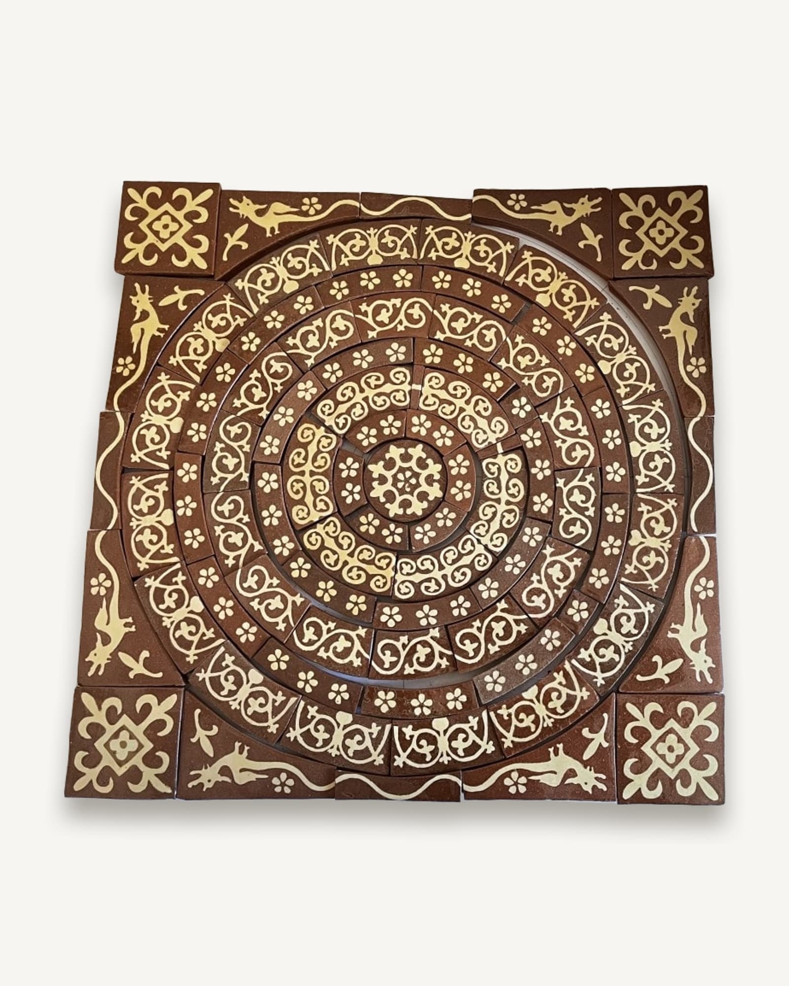 Finished roundel of curved red tiles inlaid in white scrolls and flowers, squared off by corner tiles of long-tailed beasts