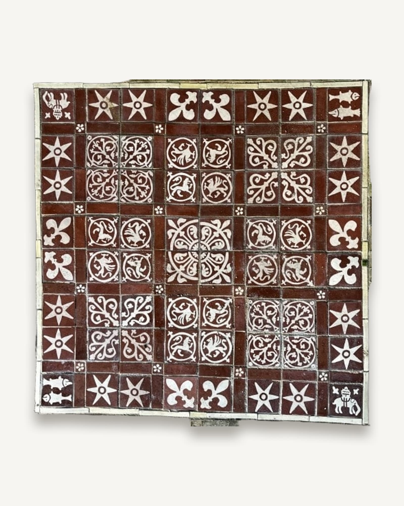 Square panel of red and white inlaid floor tiles: stars, fleur-de-lys, pike and beasts in roundels around a four-tile centre
