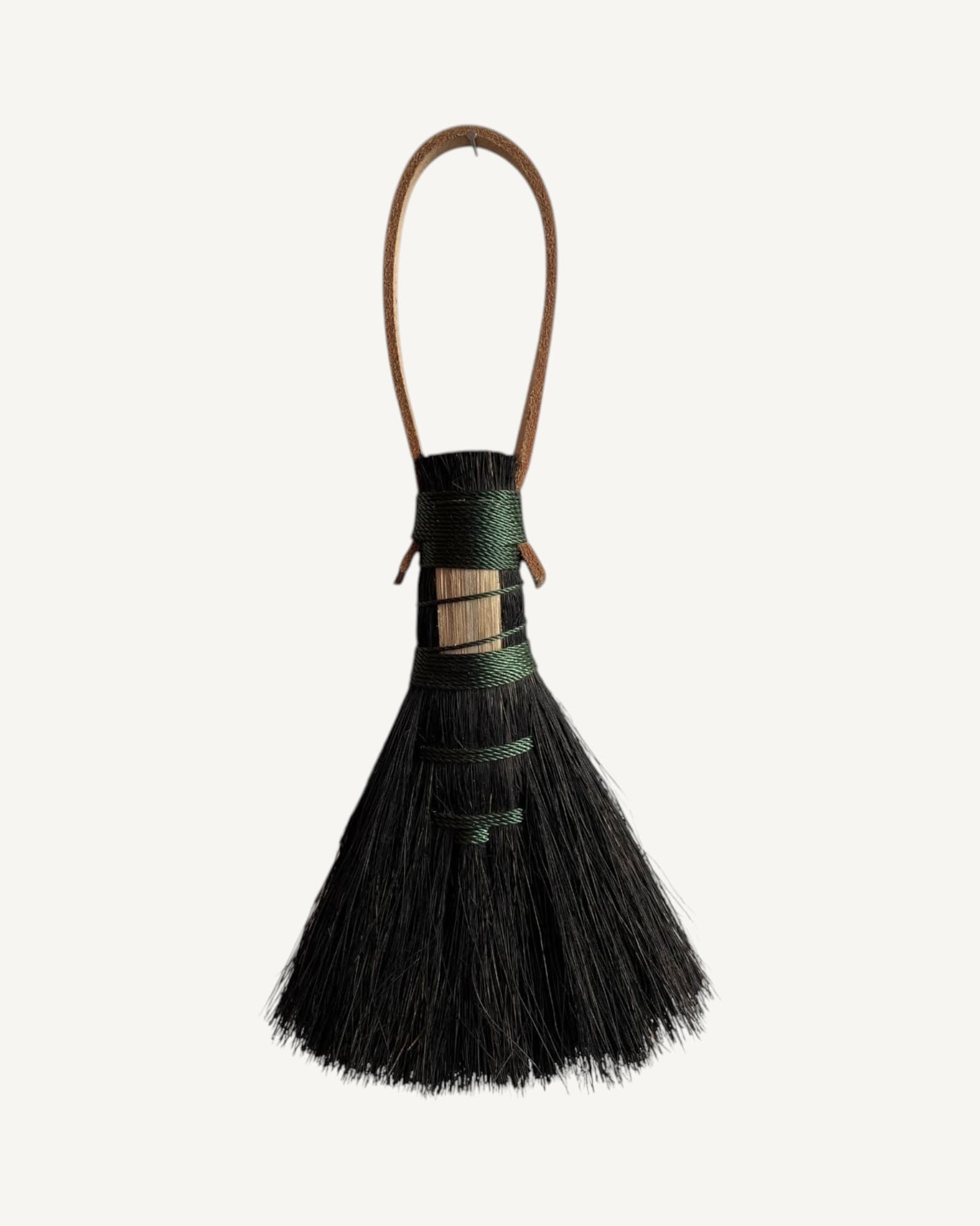 Black arenga fiber brush head with natural wood inset band, bound with green twine, attached to brown leather loop handle.