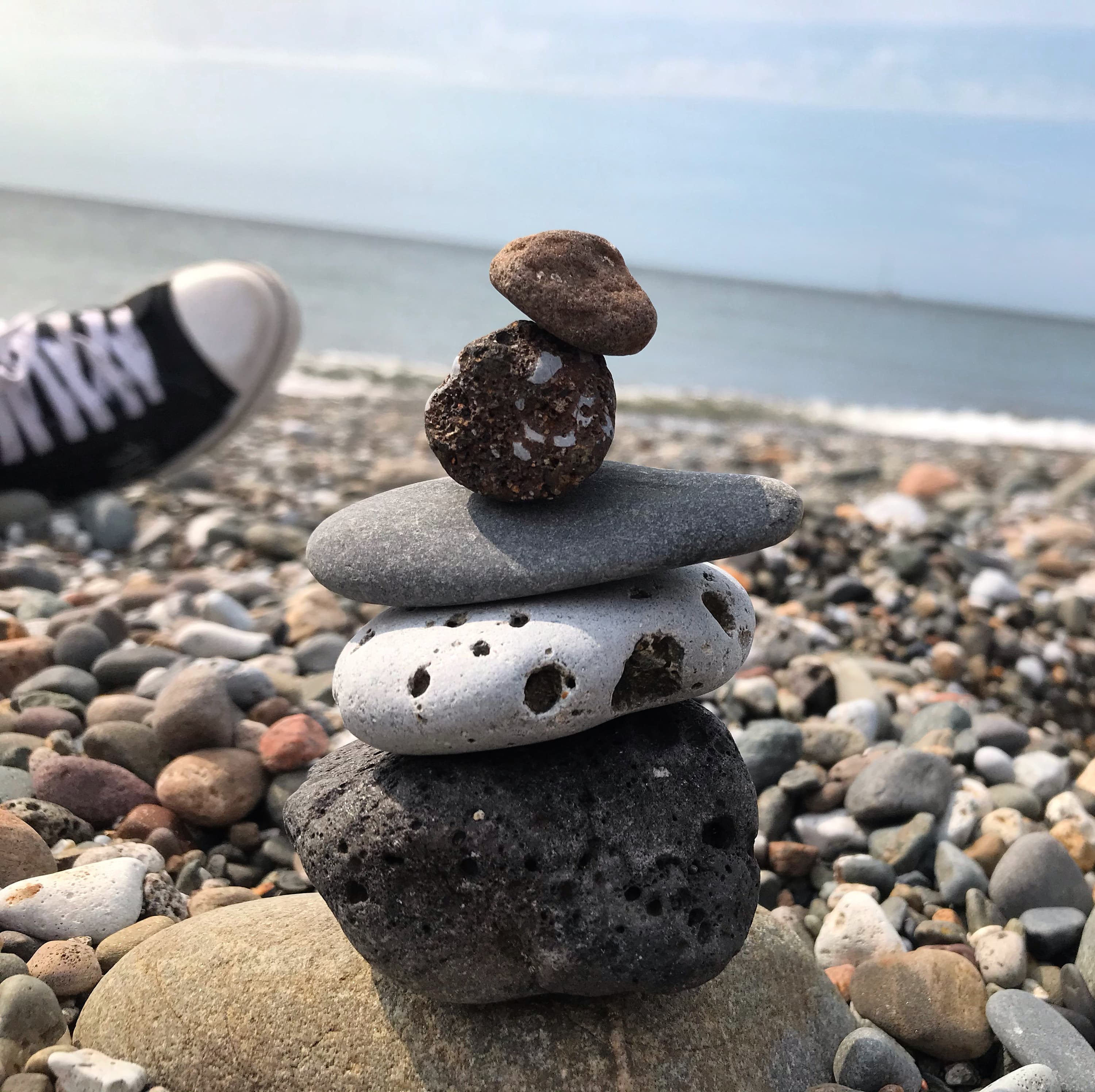 Stacked pebbles on a shingle beach with the sea behind, a trainer at the edge of the frame