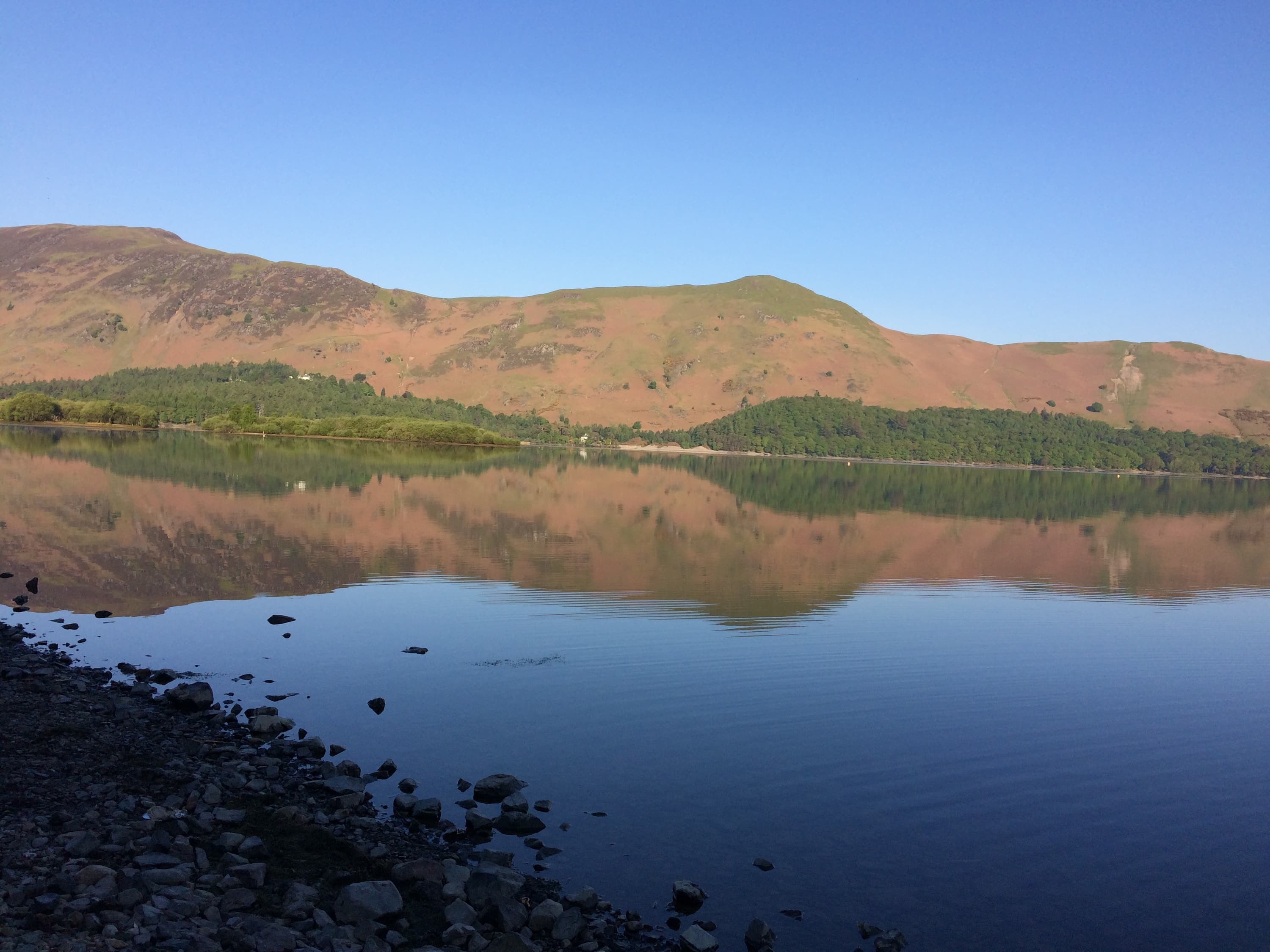 Still lake with fells reflected in the water under a clear blue sky