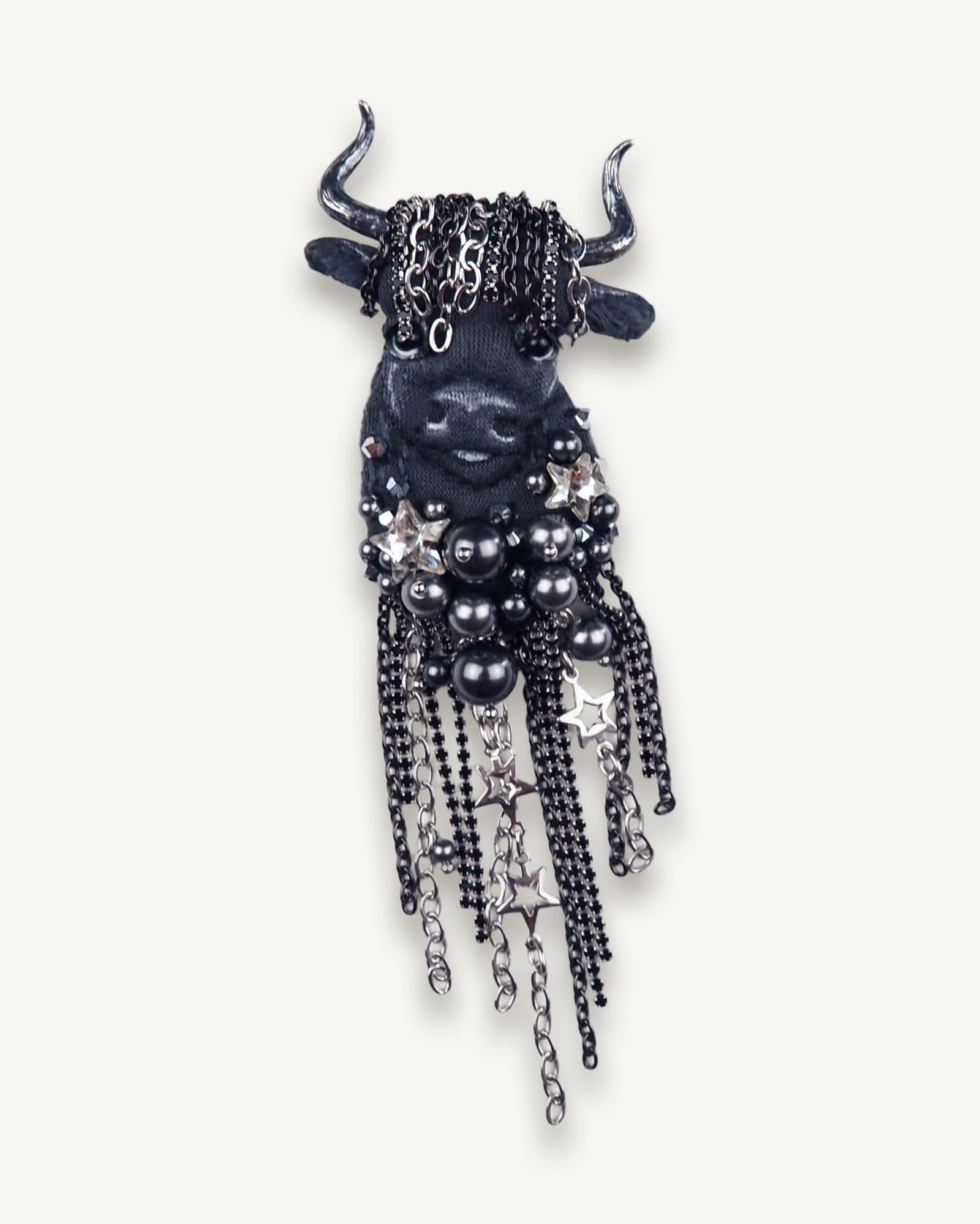 Close-up of handmade Taurus textile brooch featuring black embroidery, custom horns, glossy beads, and chain fringe with rhinestones