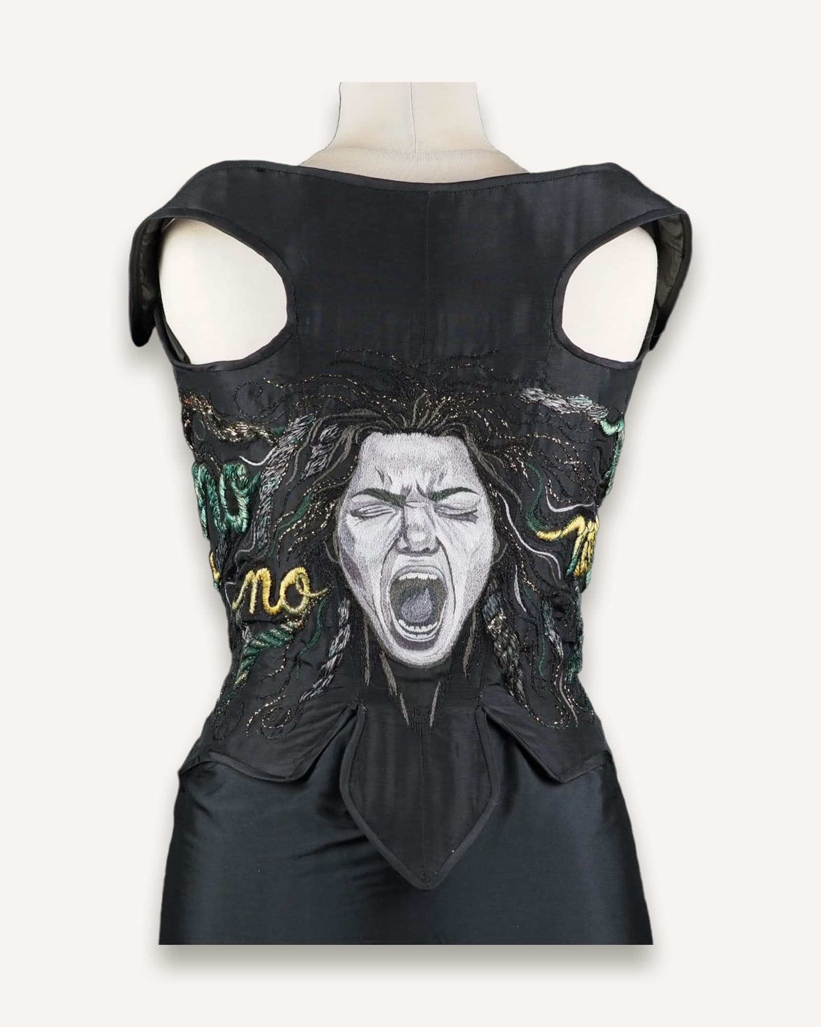 Black taffeta corset with hand-embroidered Medusa face and rope-like hair forming the word “NO” across the back, displayed on mannequin.