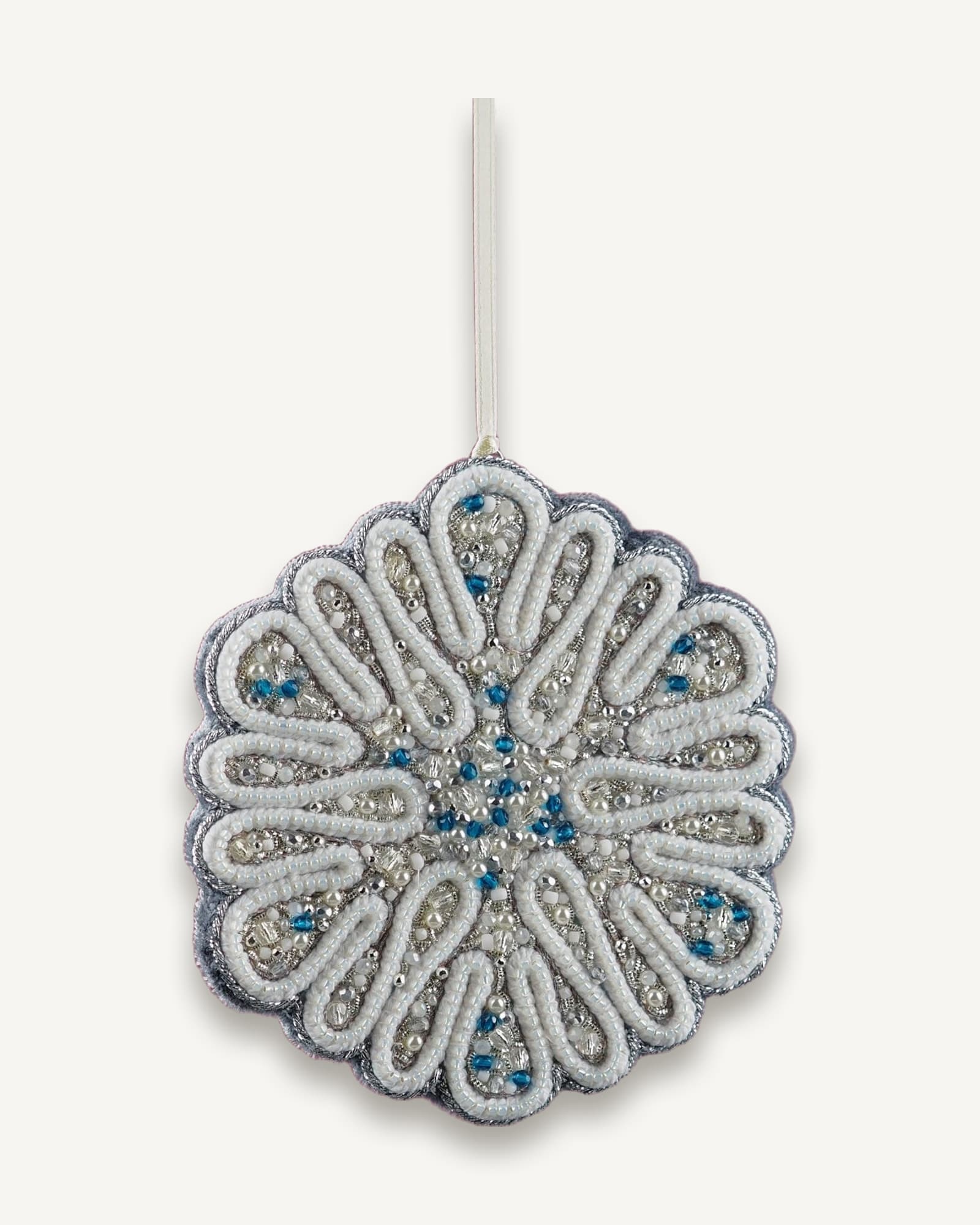 Hanging view of the Jewels of Winter circular snowflake ornament by Ksenia Semirova, crafted with pearl-setting technique in white, silver, and blue tones. Shown suspended on a satin ribbon against a pink background.
