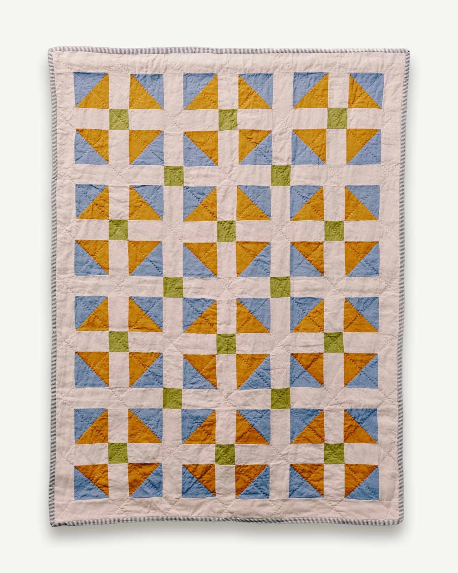 Patchwork cot quilt with repeating geometric blocks in blue, golden yellow and olive green on cream linen