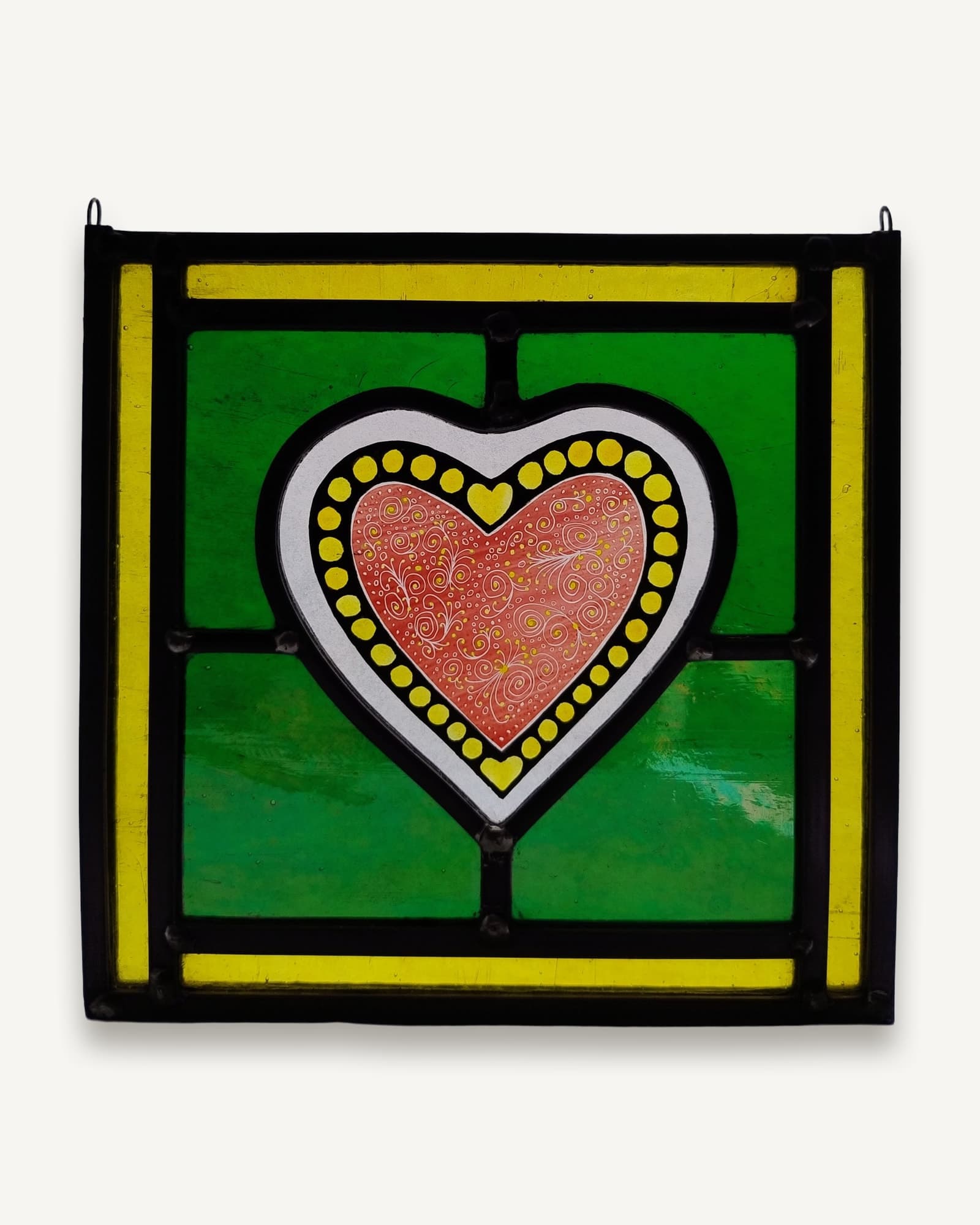 A coral heart painted with fine white tracery, ringed in yellow dots on a bright green leaded ground.