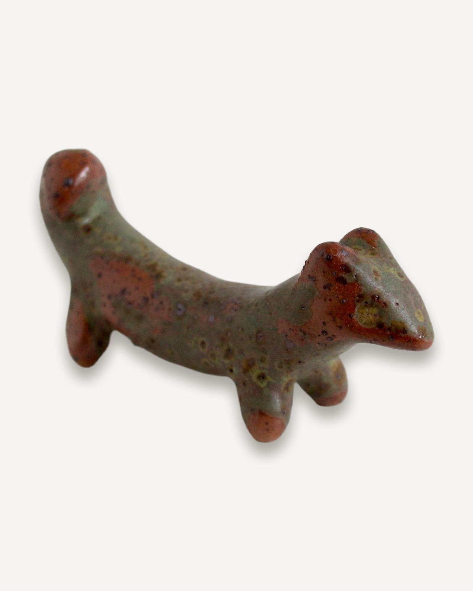 Pinched stoneware hound stretched horizontally, glazed mossy green with rust-red speckles and lichen-like surface texture