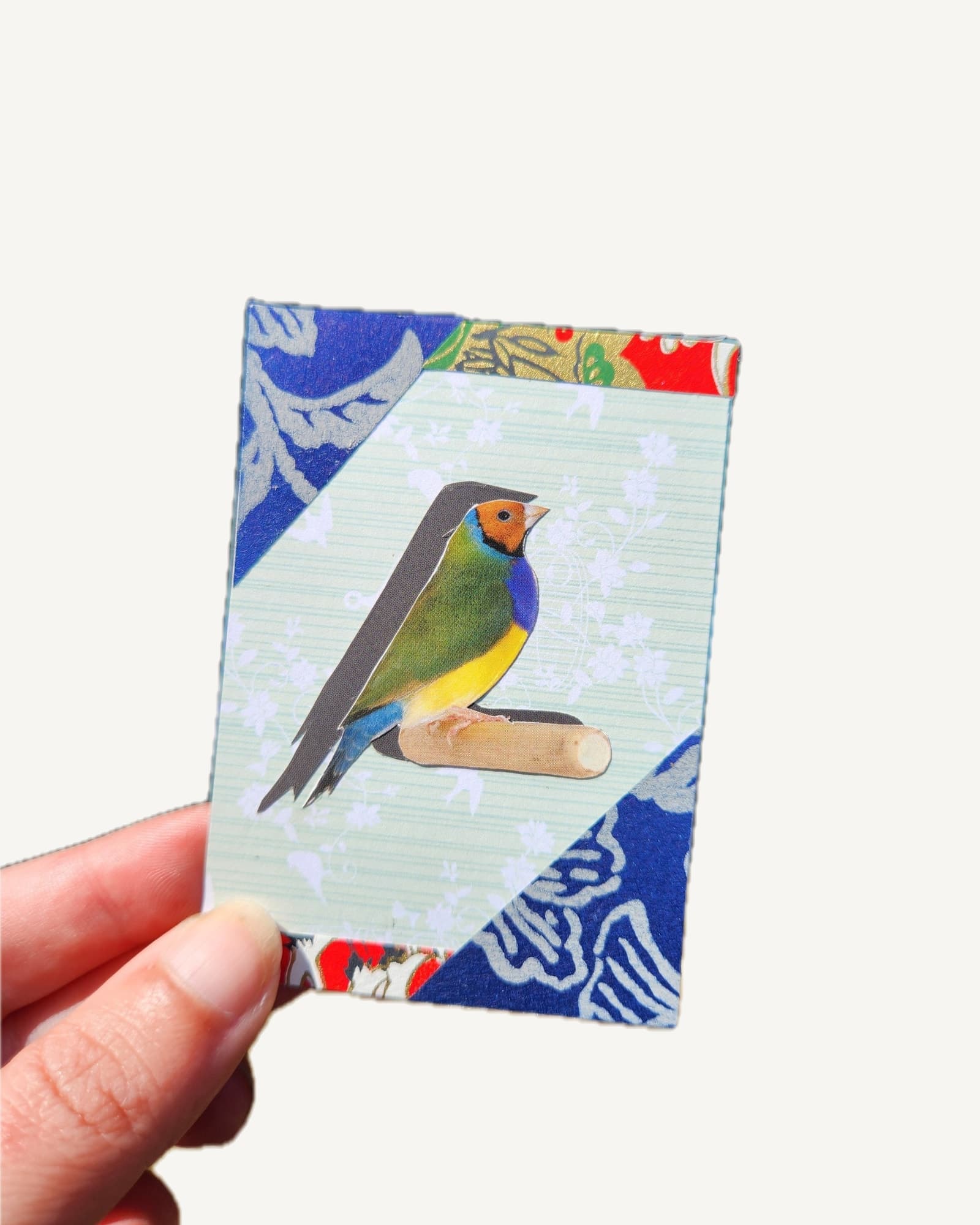 A yellow-headed Gouldian finch cut by hand from a secondhand bird book, on mint card with royal blue and gold origami paper.