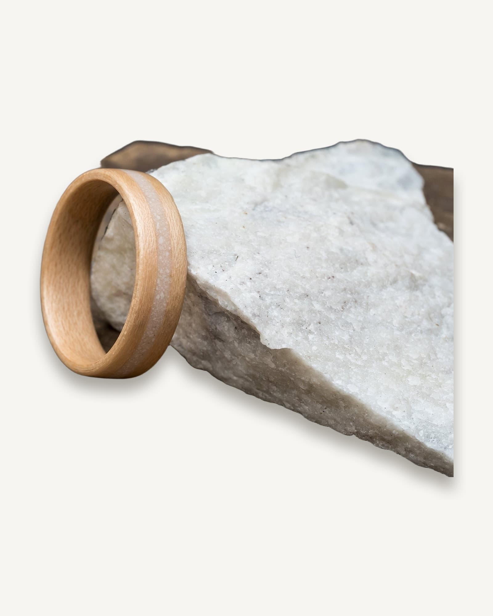 Polished ash bentwood ring with inlaid white and grey marble, displayed on a rough marble stone against neutral background.