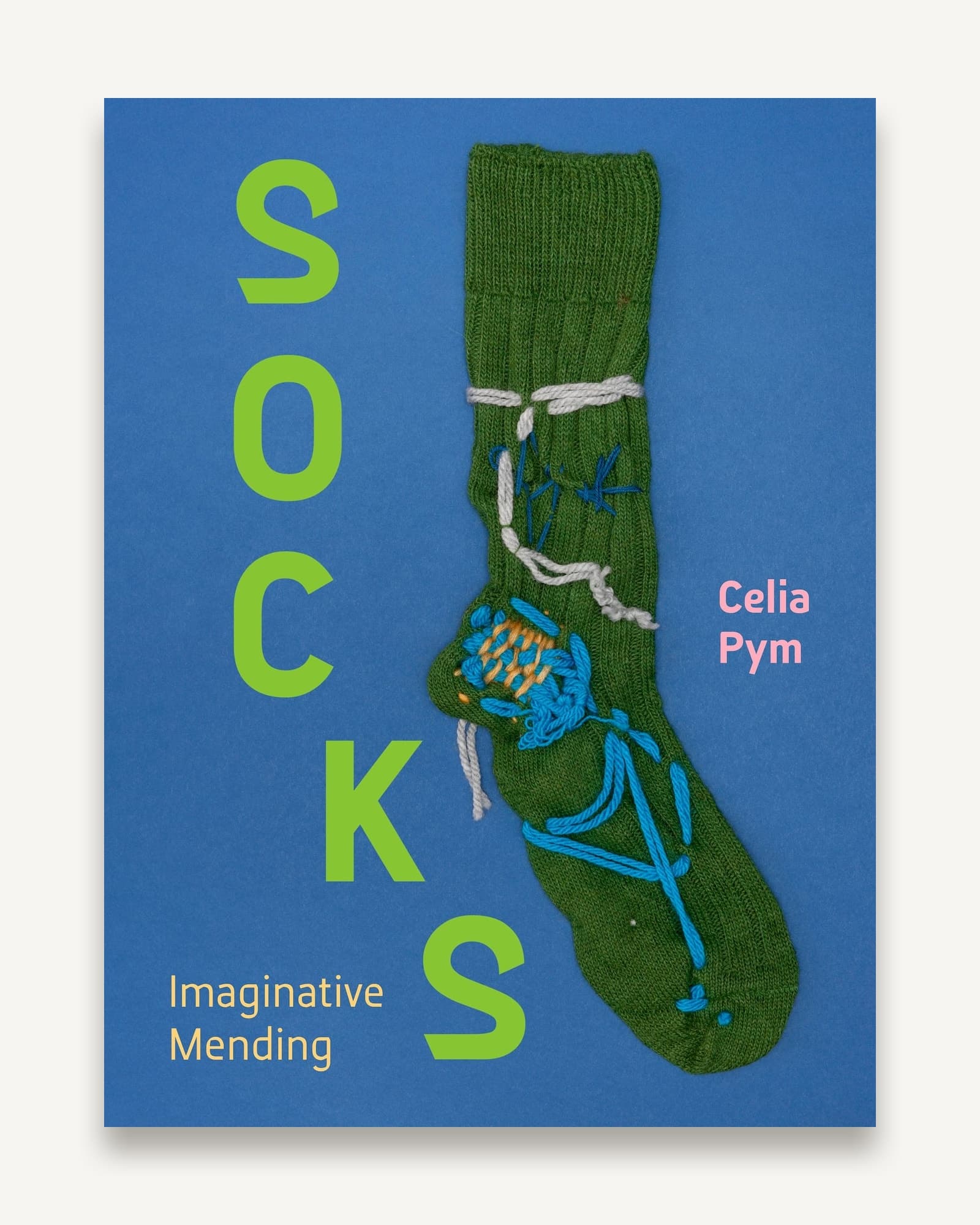 Book cover with bright blue background, green knitted sock decorated with colourful embroidered darning in blue and orange
