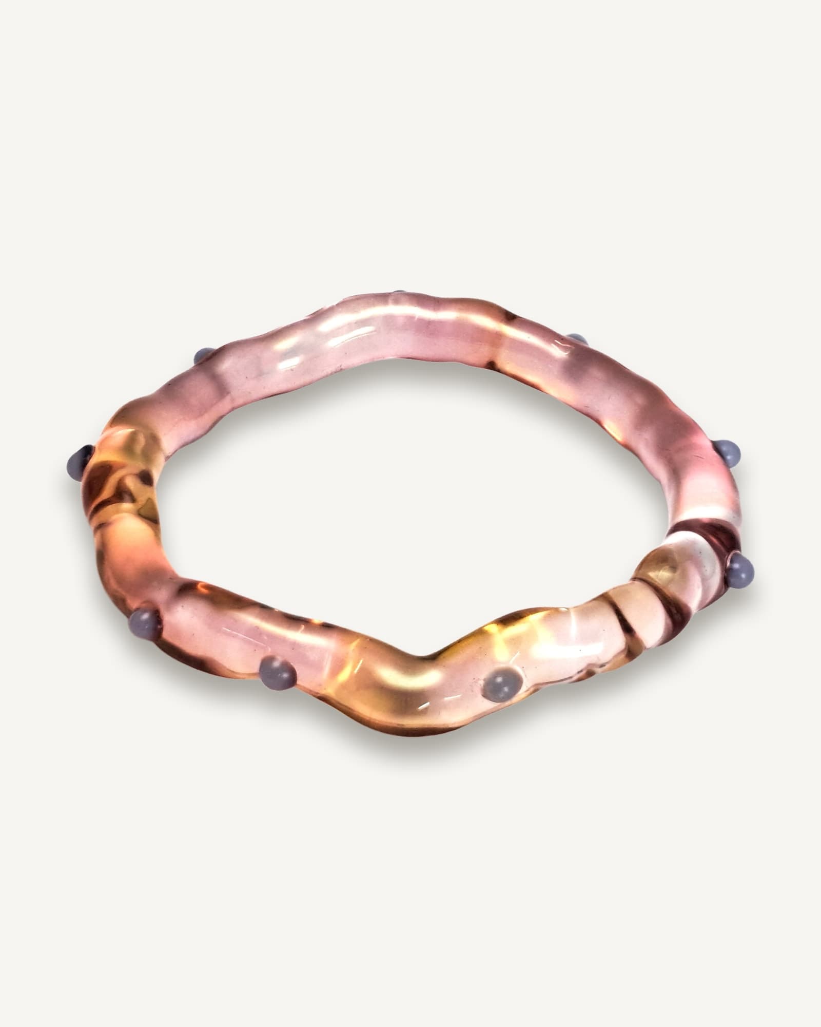 Translucent glass bangle with pink and gold tones, studded with small opaque blue beads at intervals around the curved