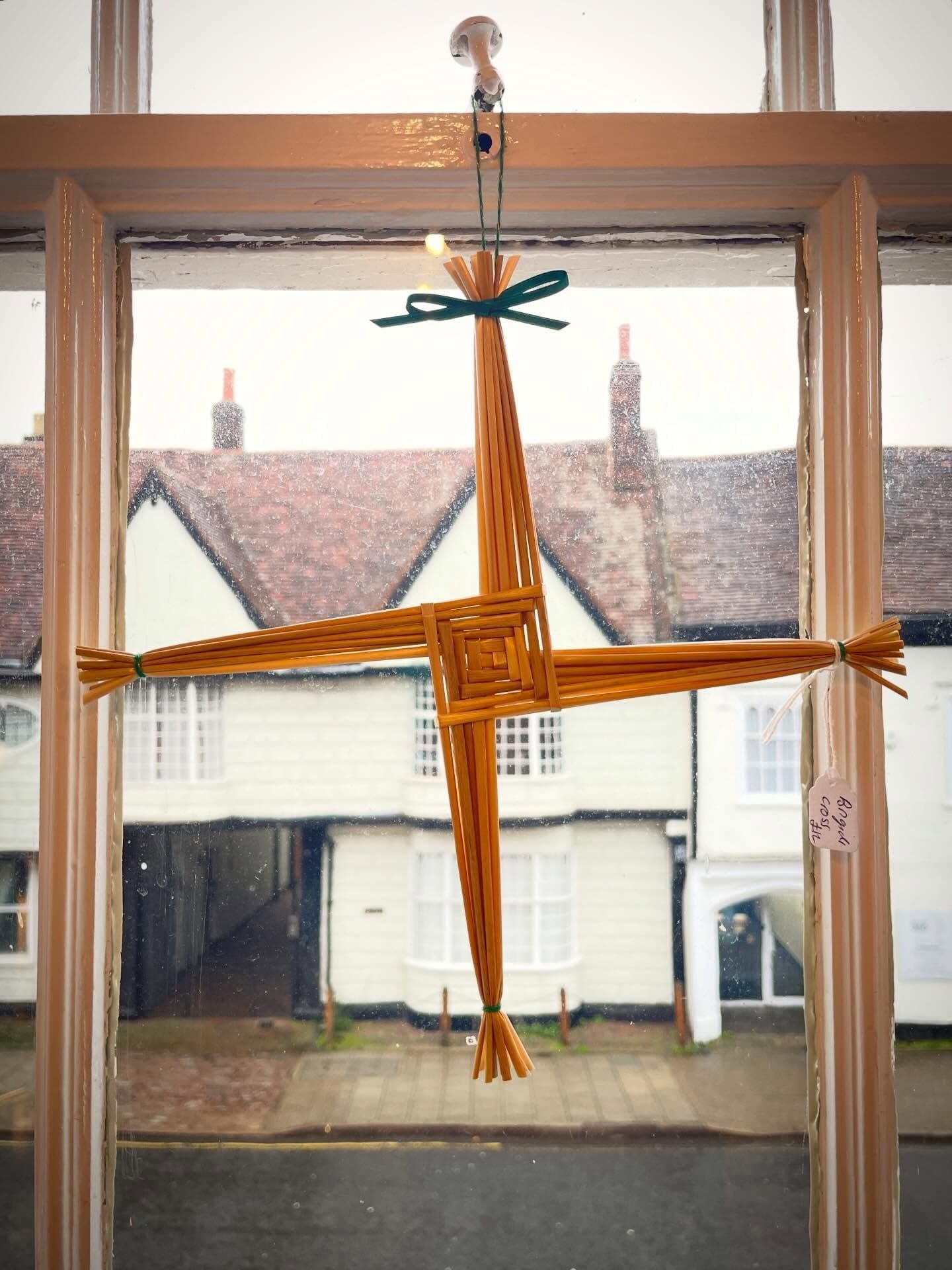 A straw cross with a green ribbon hanging in a window overlooking a street of old houses