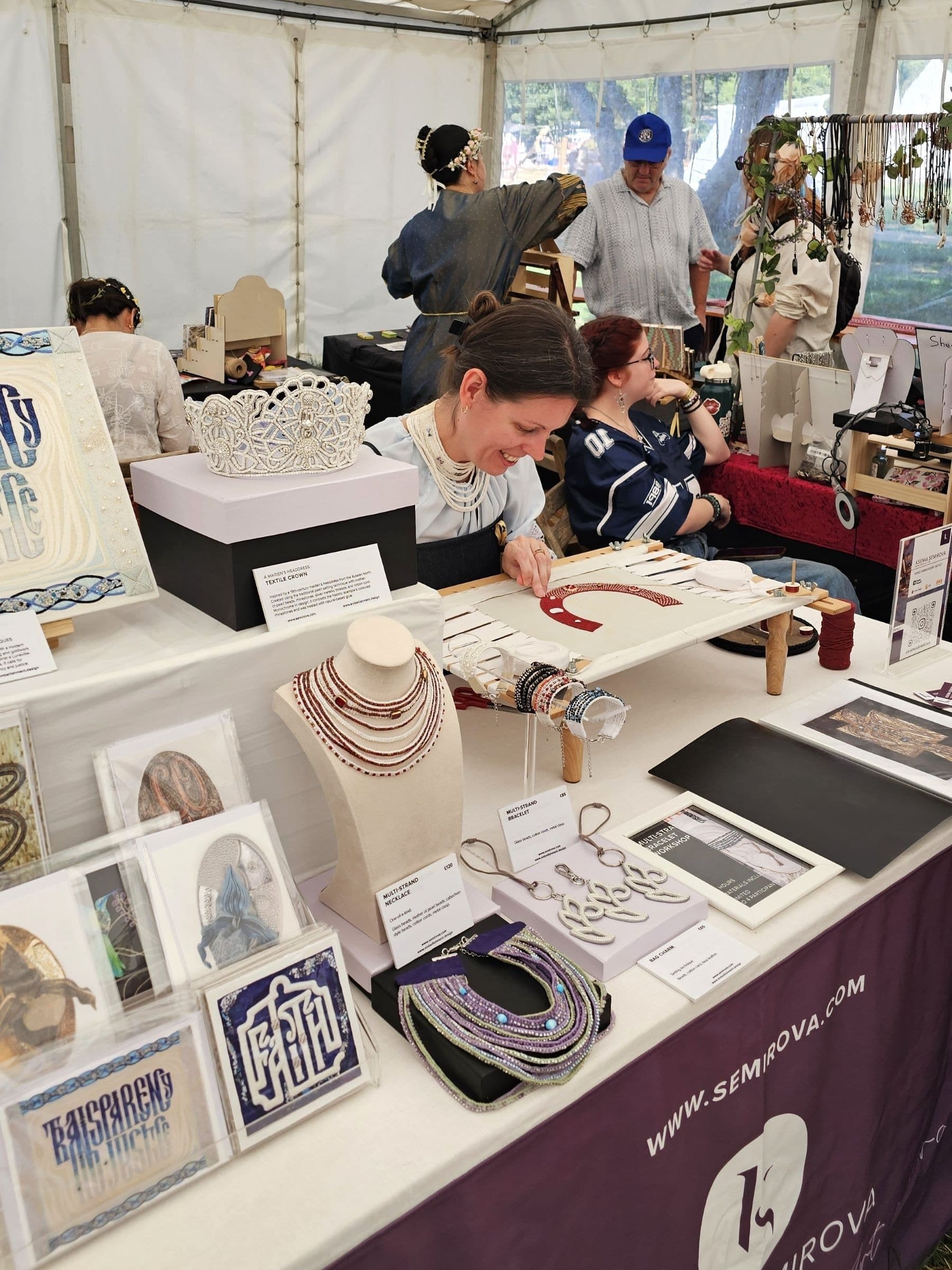 Craft market stall displaying embroidered jewellery, beaded necklaces in cream and red, embroidered accessories