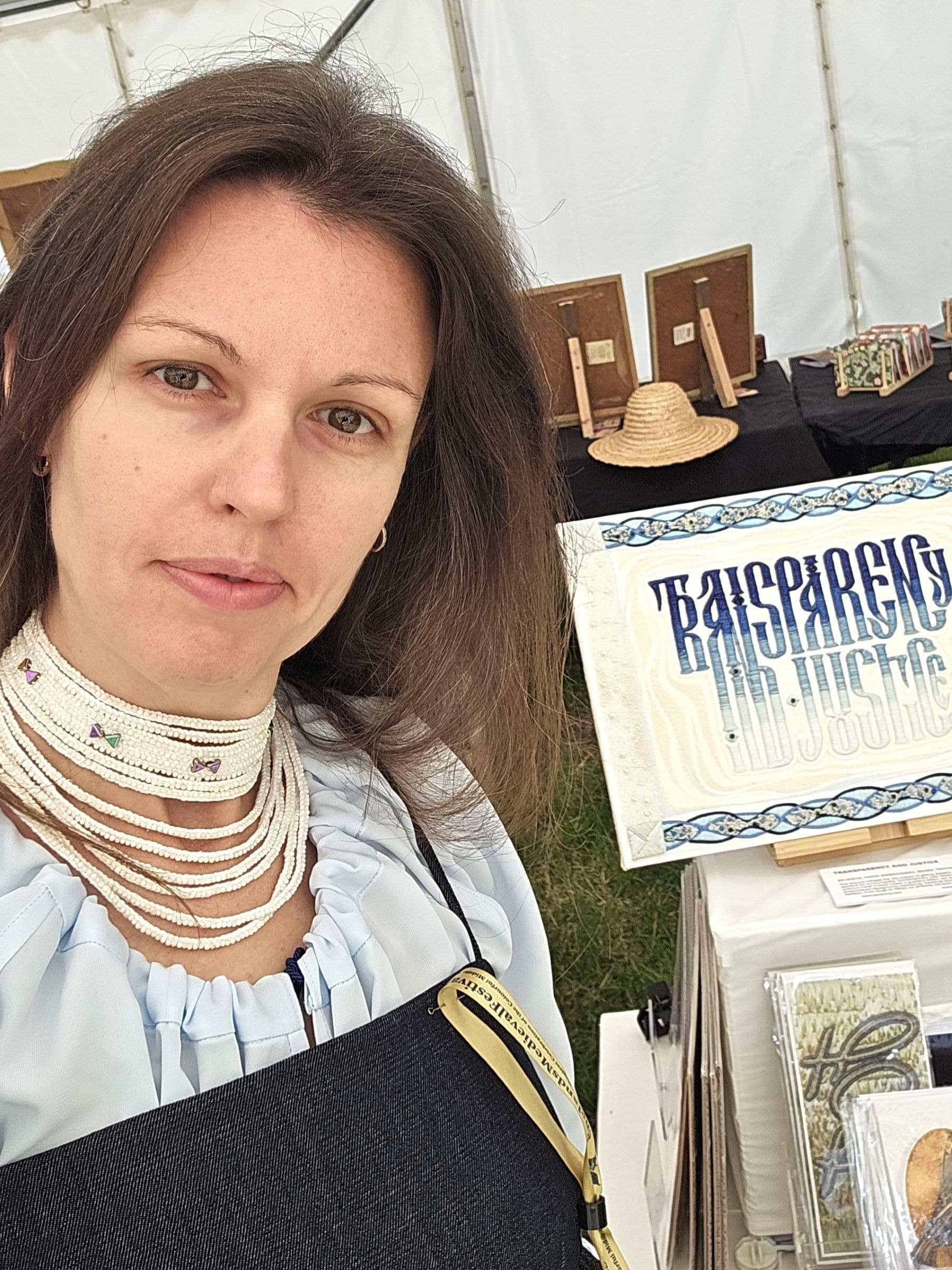 Woman at craft fair display wearing layered pearl necklaces and embroidered white blouse