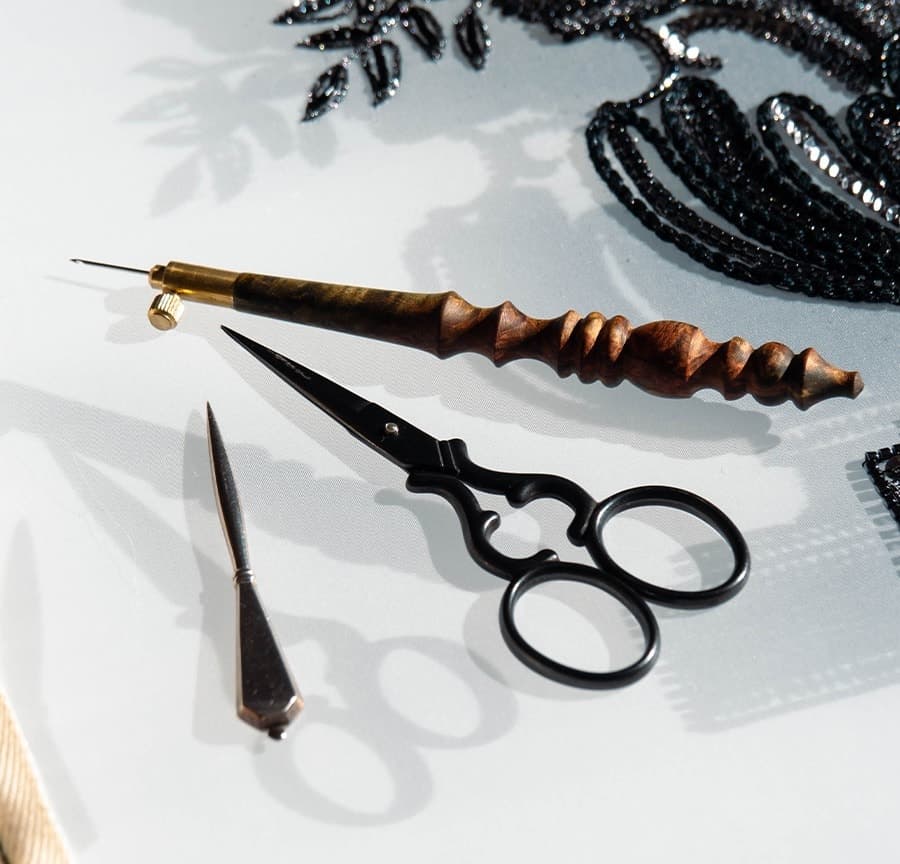 Embroidery tools arranged on white fabric: wooden handled tambour hook with brass tip