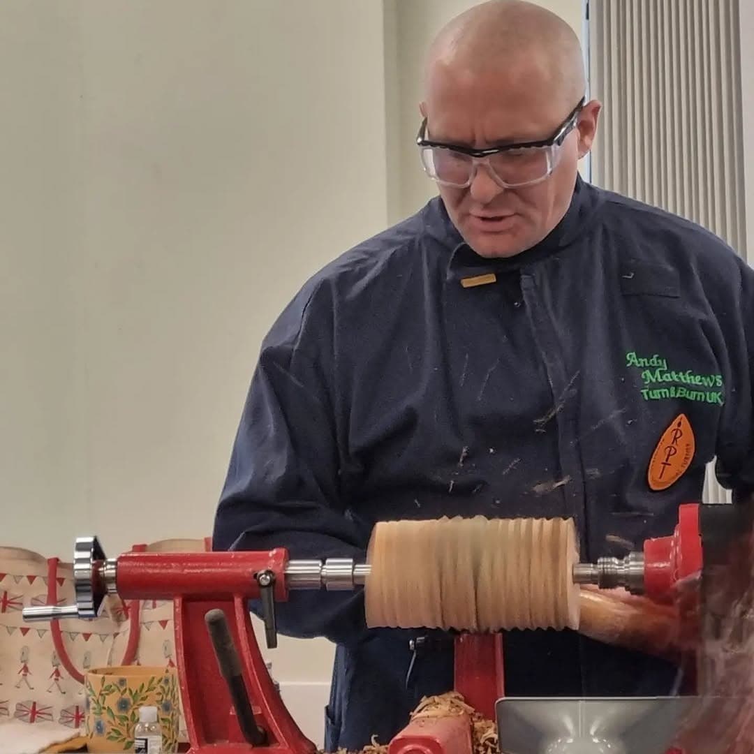 Andy Matthews turning a pale blank at a lathe in a workshop, shavings coming off the tool.