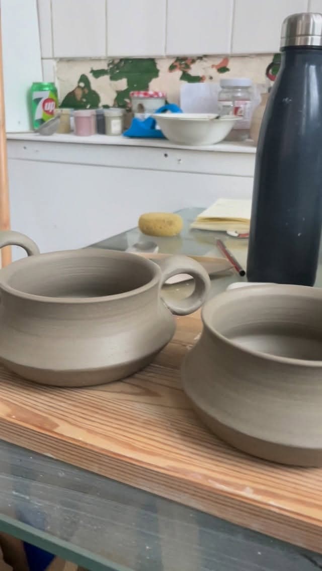 Two pale grey bowls with handles sit on a wooden surface.