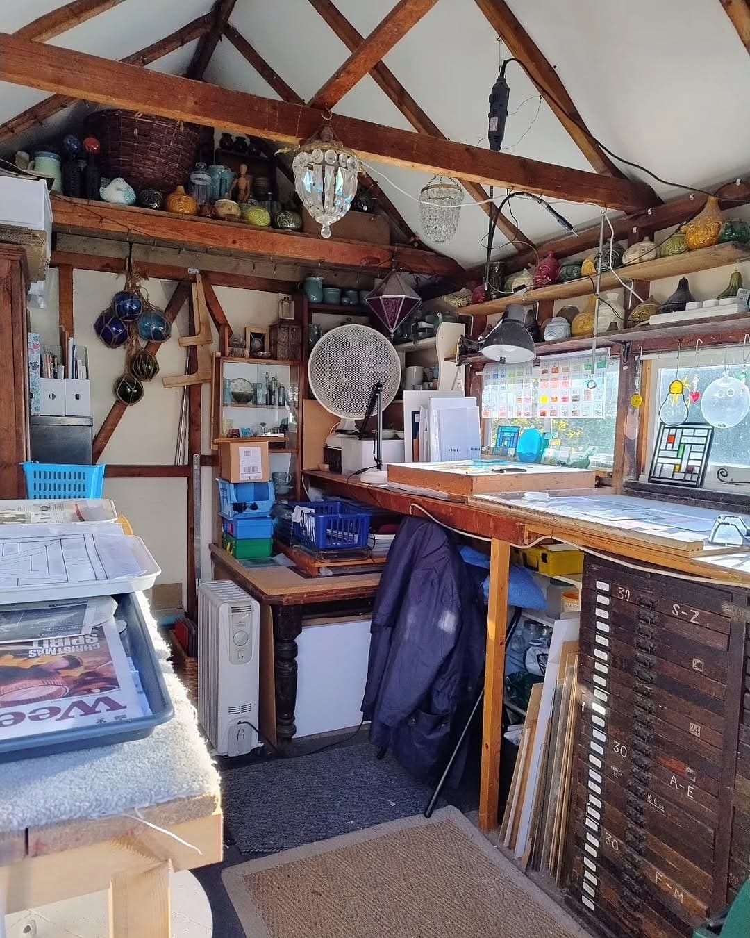 The inside of Mary Corkery's garden workshop, with open roof beams, workbenches and a plan chest of glass.